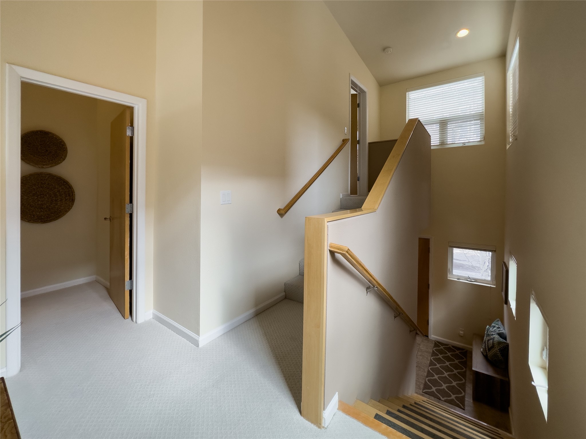 Two-story stairwell with light carpet, wood handrails, and windows with blinds.