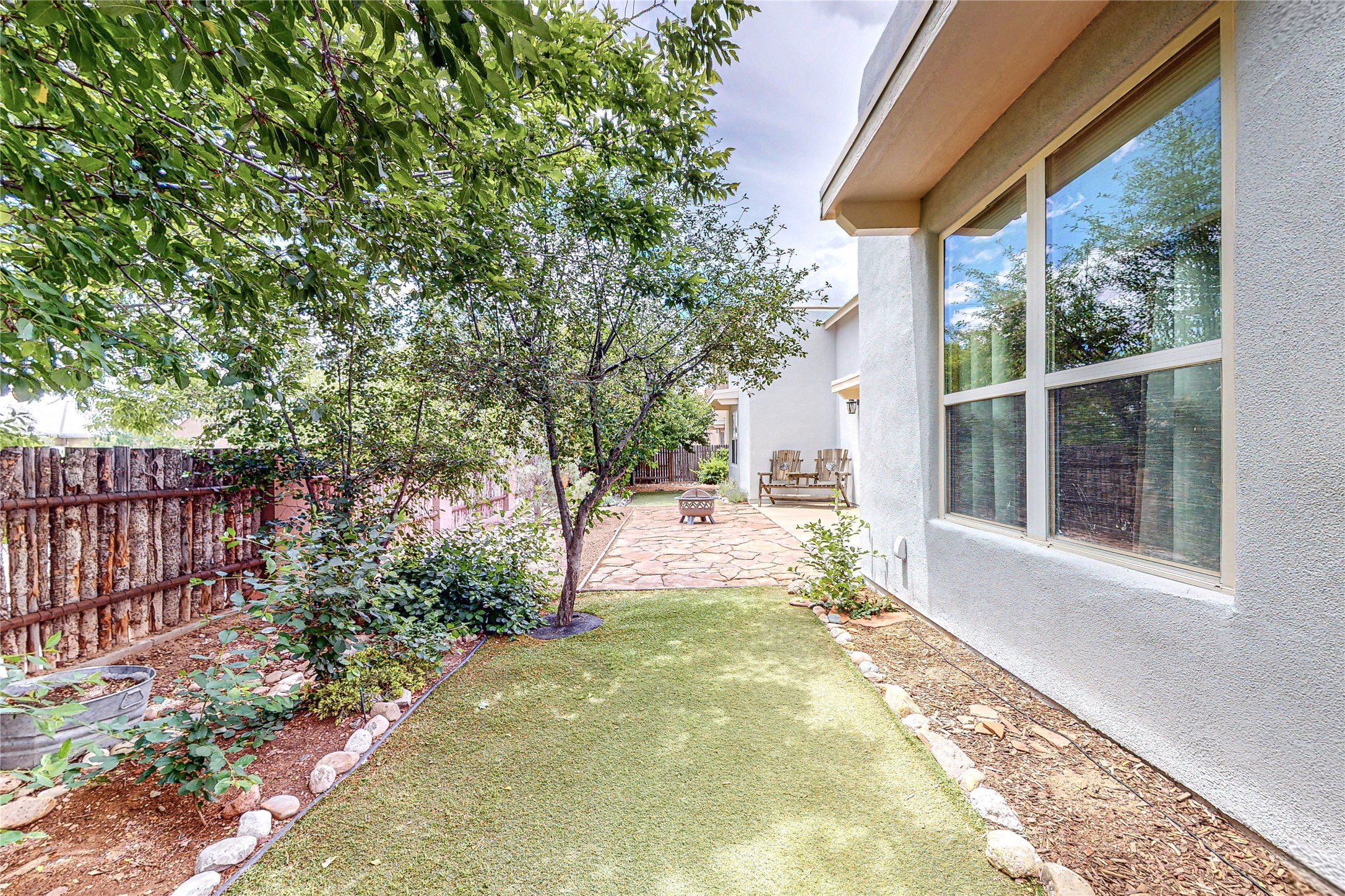 Backyard with a stone patio, leafy trees, a small lawn, and outdoor seating beside the house.