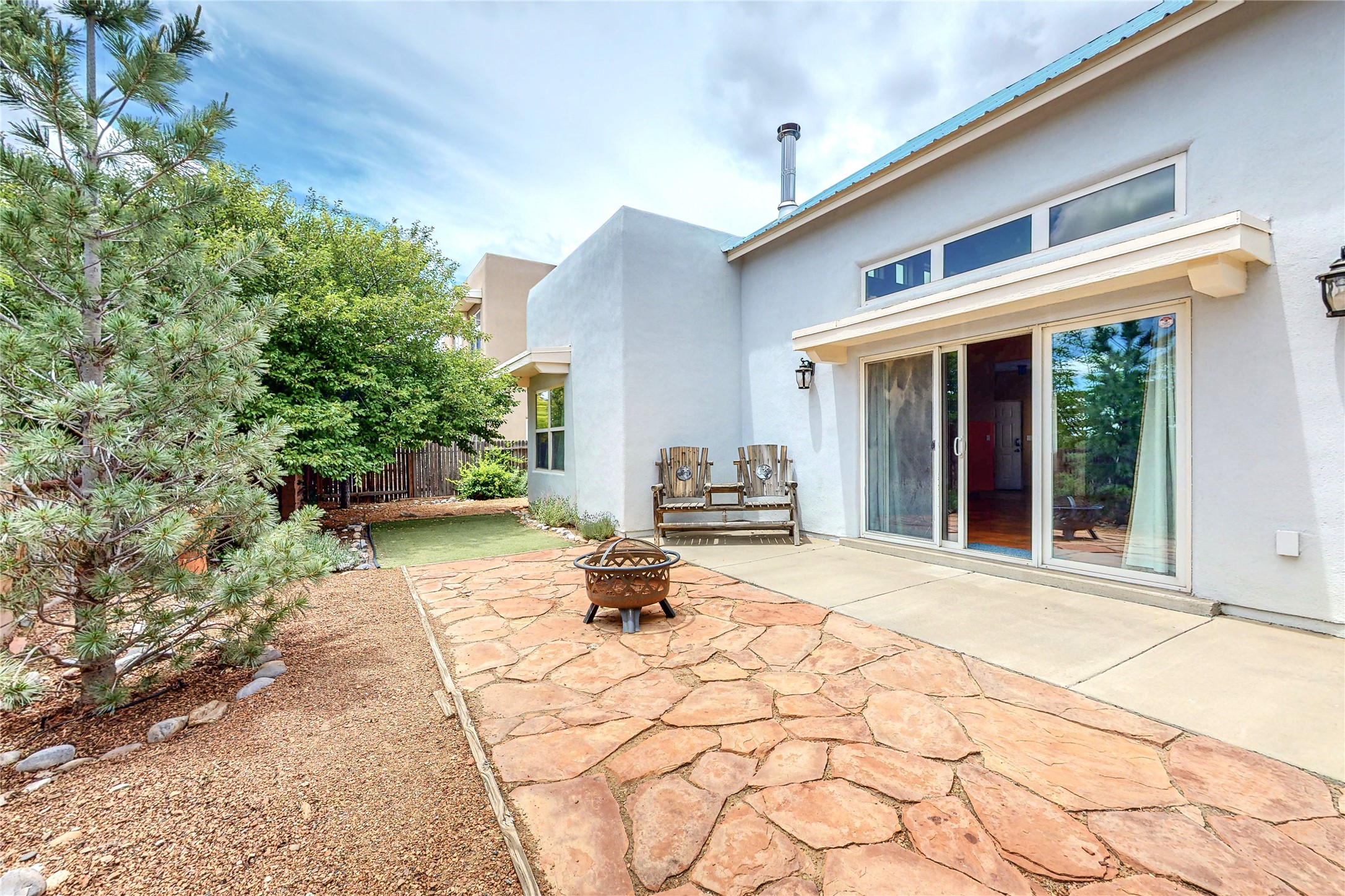 Flagstone patio with a fire pit and wooden bench beside sliding glass doors.