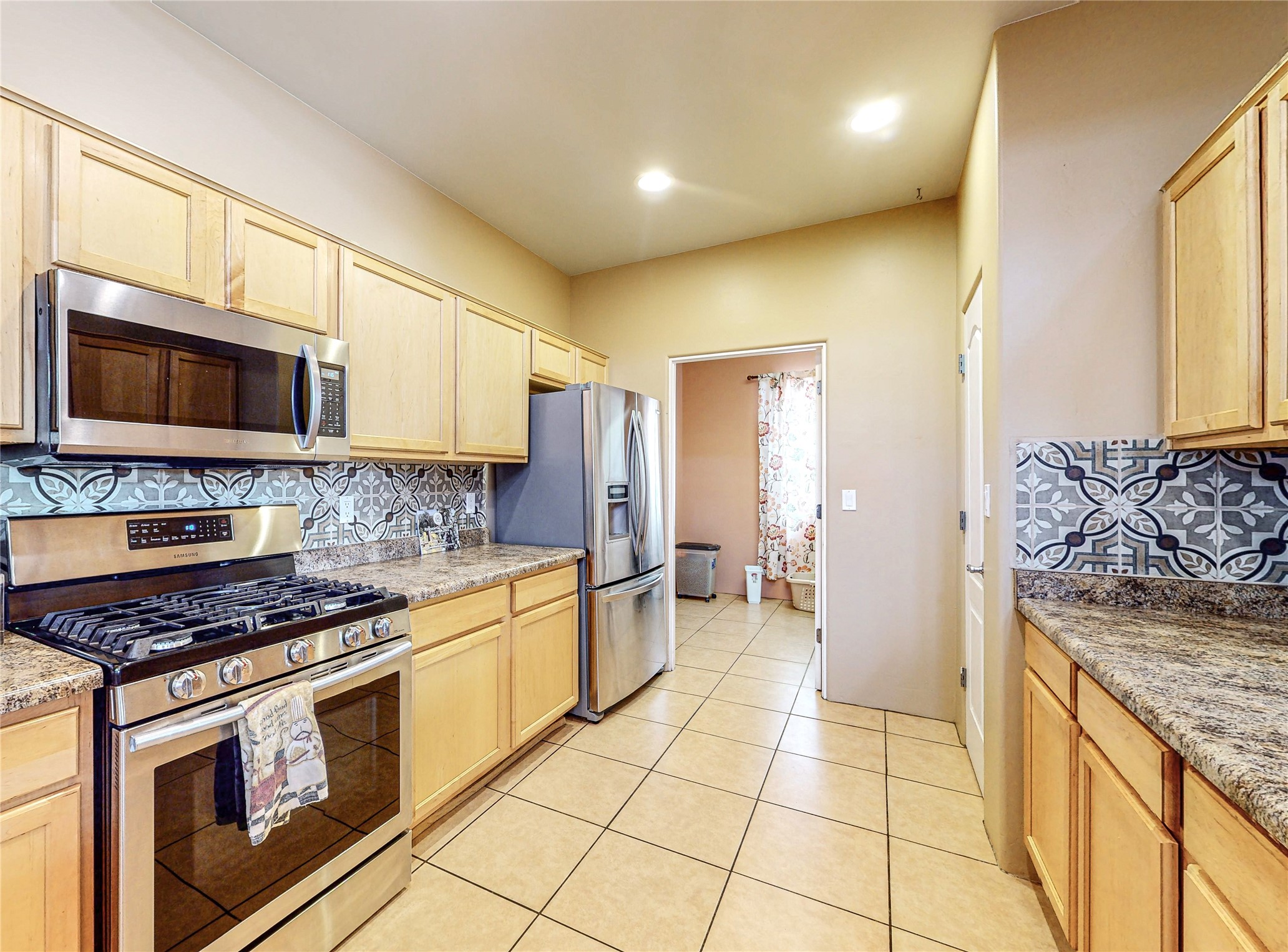 Kitchen with light wood cabinets, patterned tile backsplash, granite counters, and stainless steel appliances.