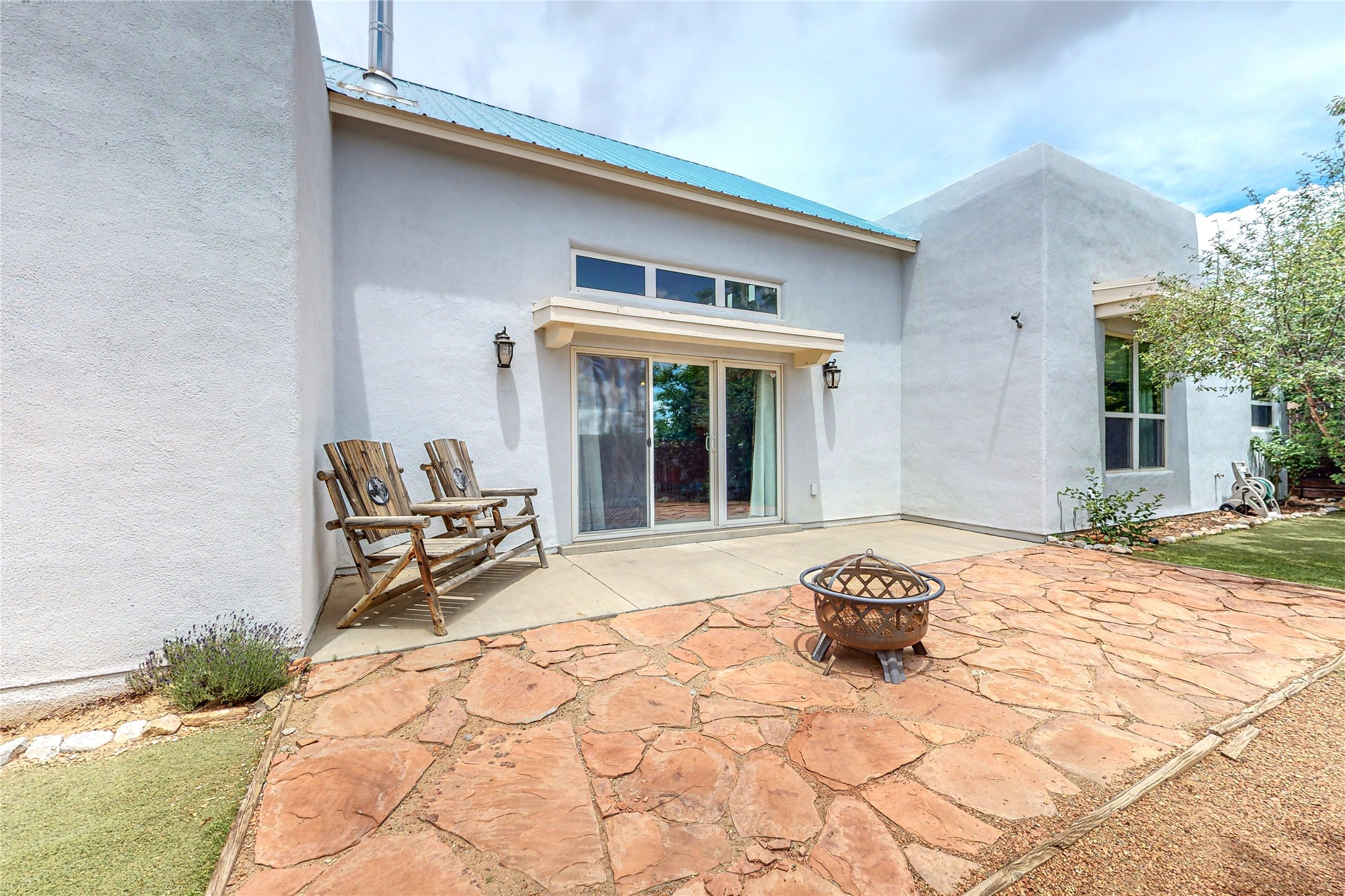 Home’s rear patio with a flagstone surface, wooden chairs, and a metal fire pit.