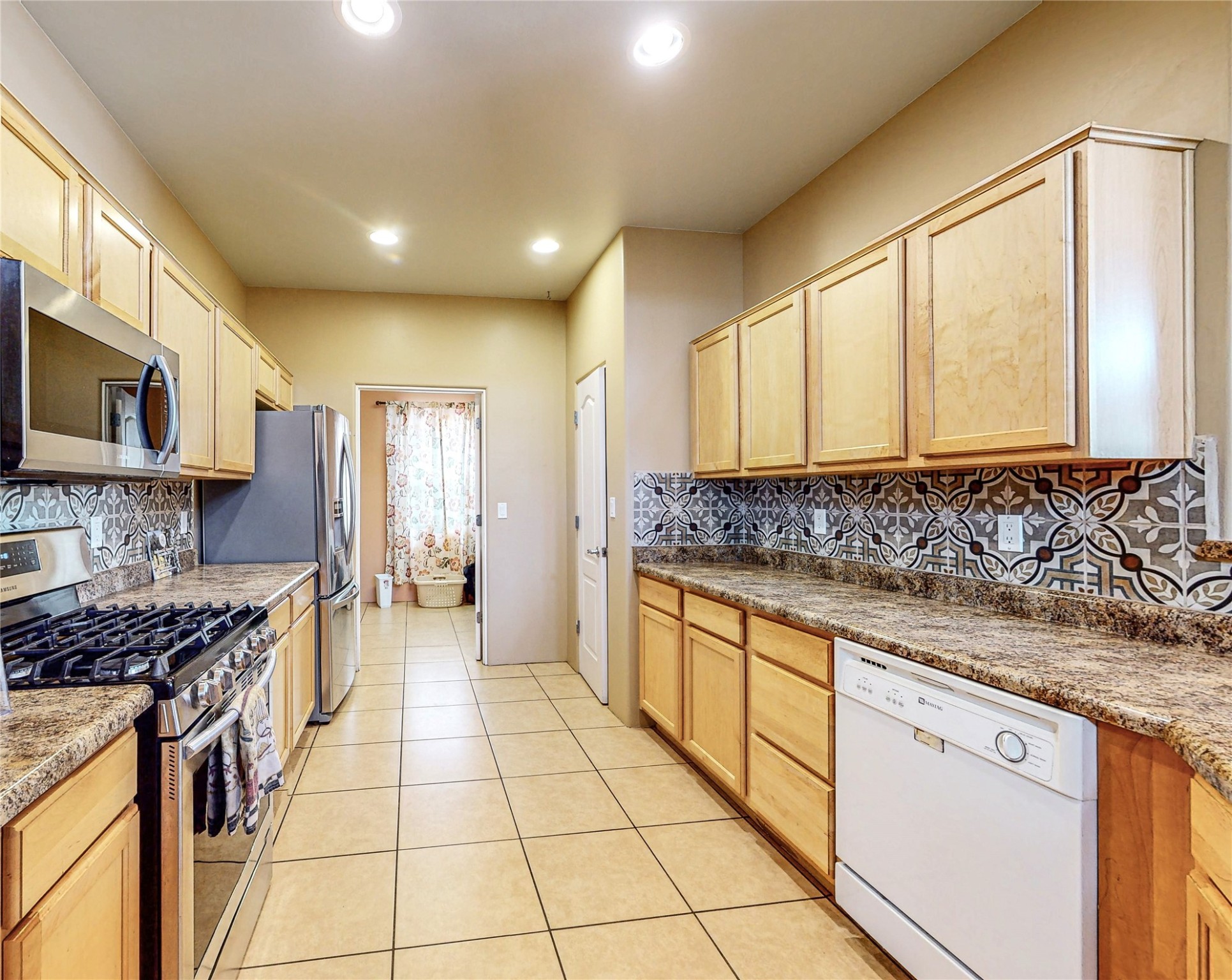 Kitchen with light wood cabinets, granite counters, and patterned tile backsplashes.