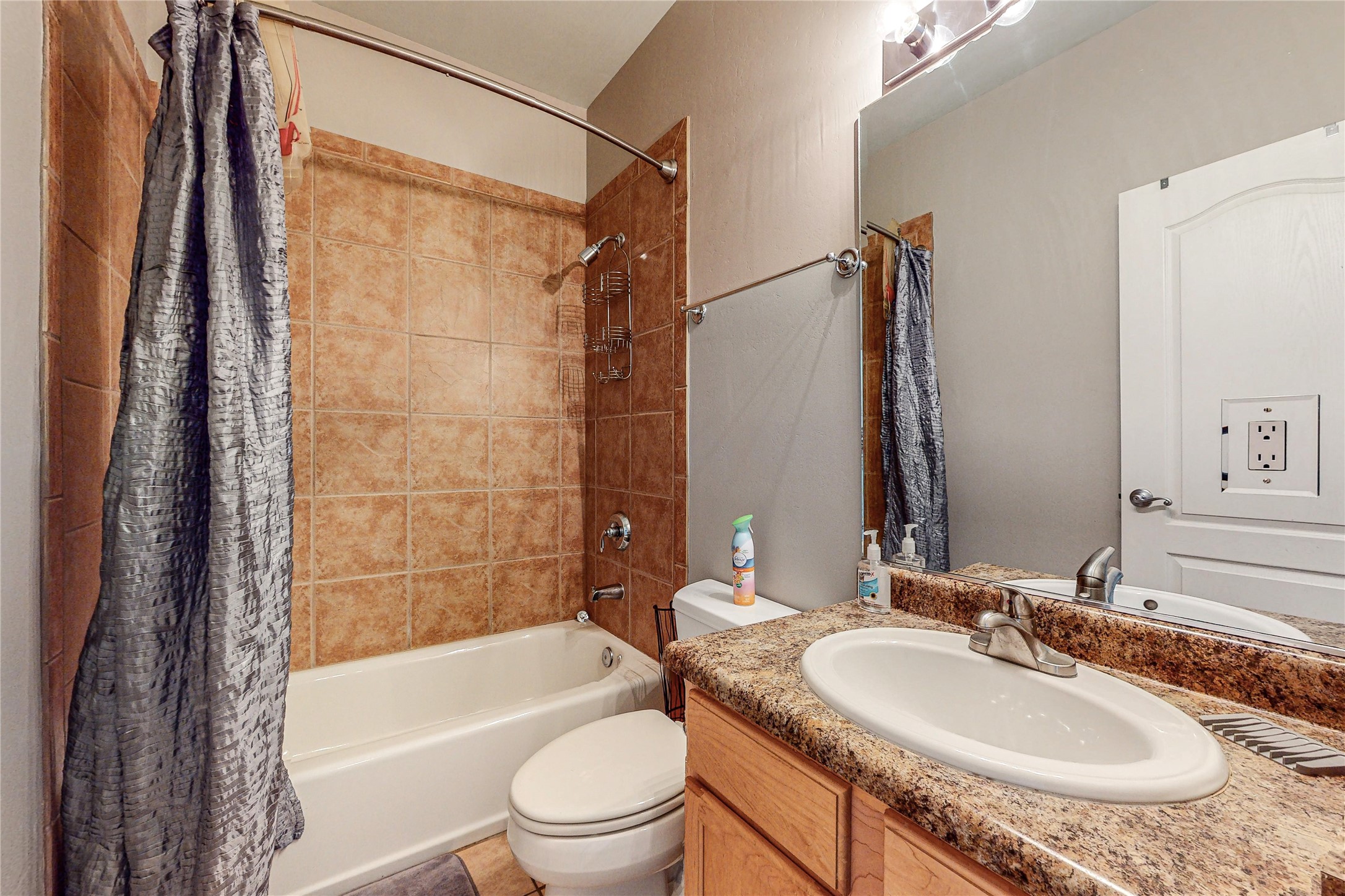 Bathroom with a tiled tub and shower beside a granite-topped wood vanity.