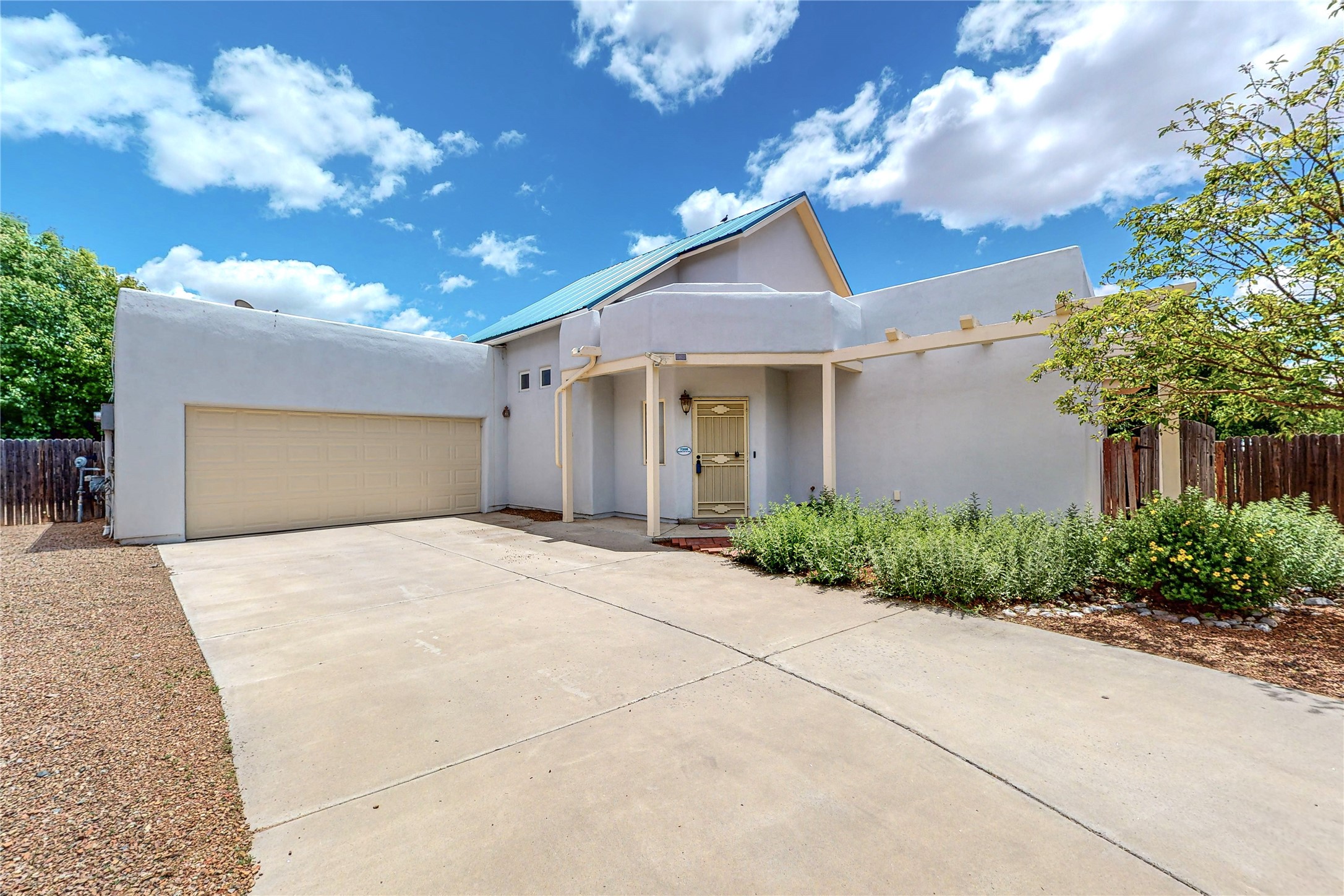 White stucco home with a blue metal roof, double garage, and covered entry.