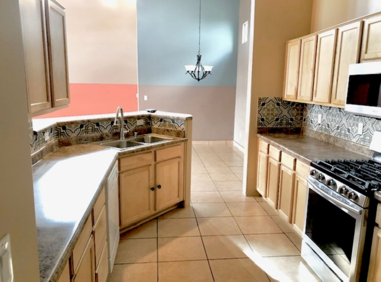 Kitchen with patterned tile backsplash, granite counters, light wood cabinets, and a stainless-steel gas range.