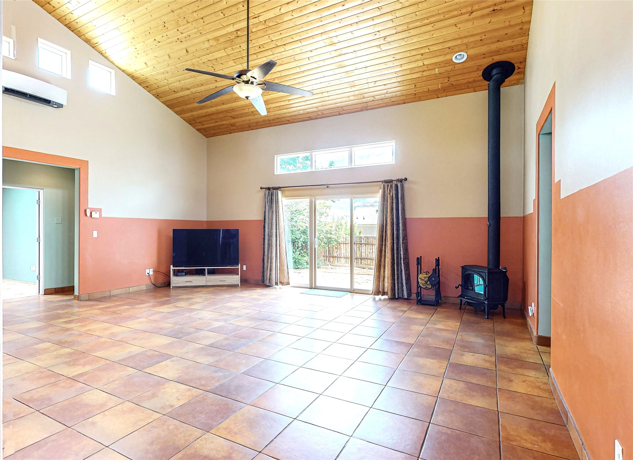 Living room with a vaulted wood ceiling, terracotta tile floor, and black wood-burning stove.