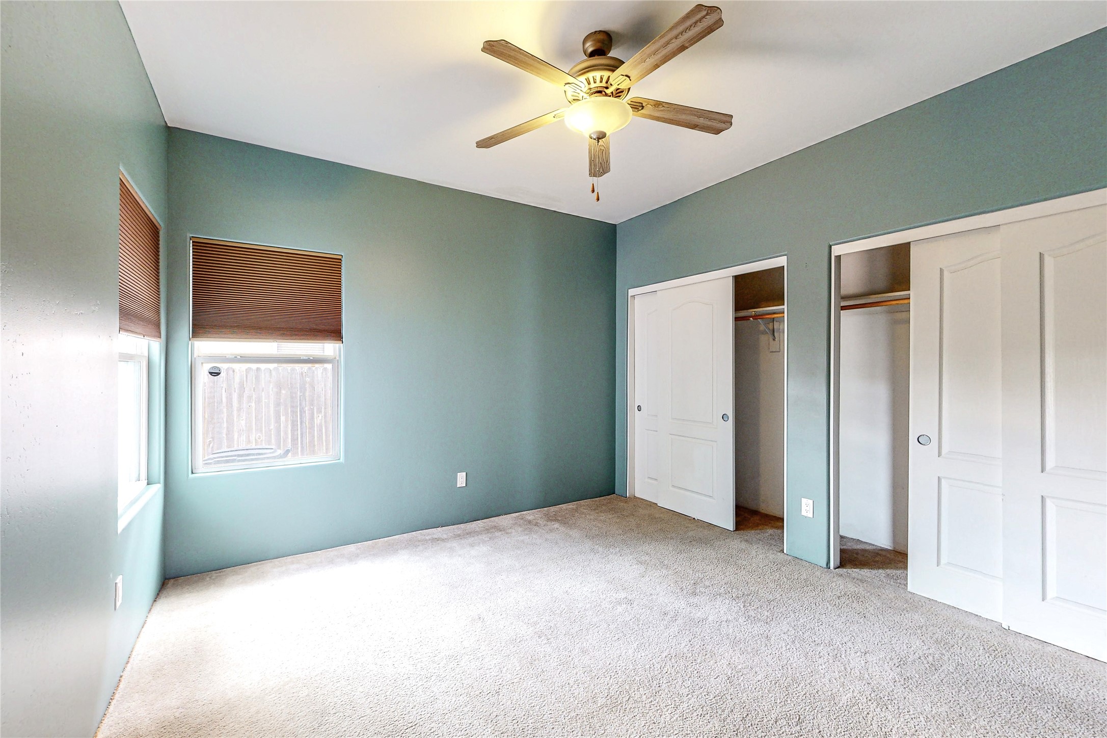 Empty bedroom with blue-green walls, carpet, a ceiling fan, and two closets.
