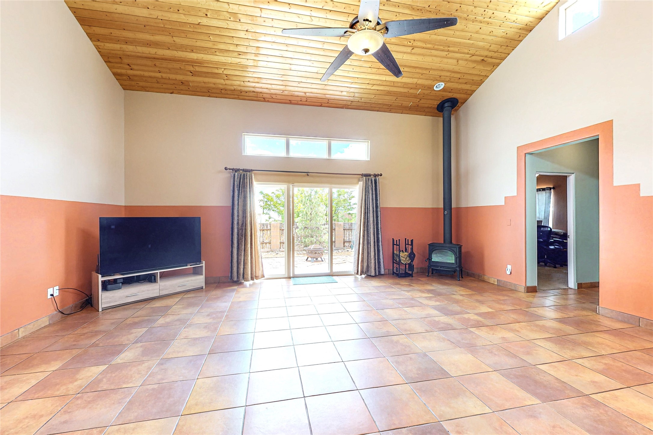 Living room with a wood-plank ceiling, tiled floors, wood stove, and sliding doors to a patio.