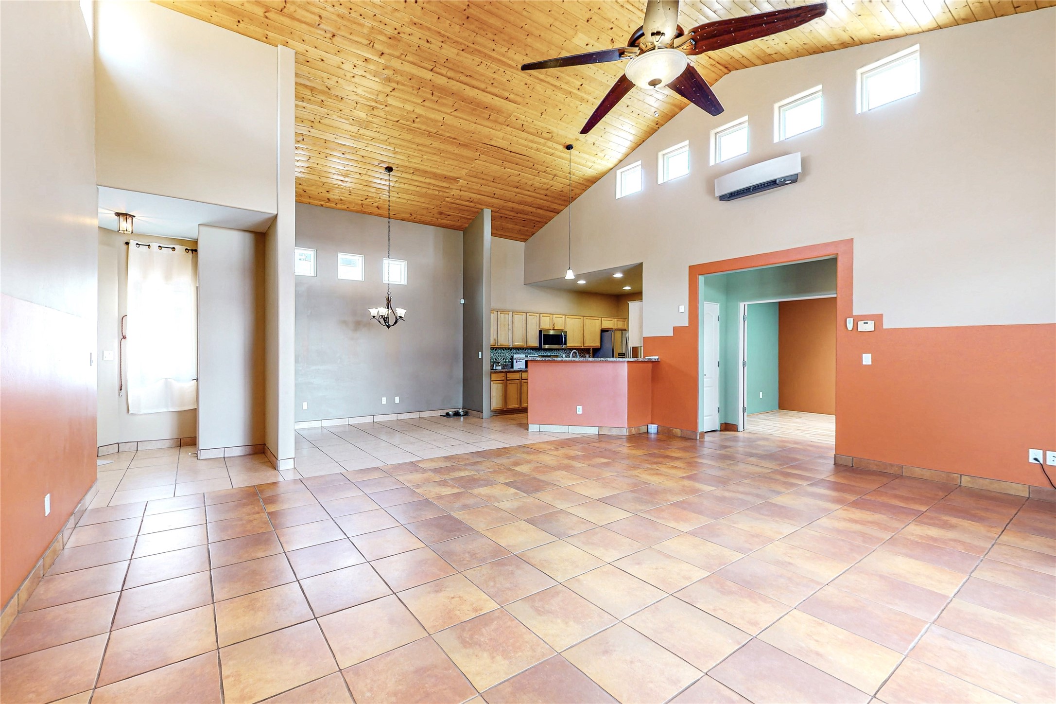 Open living and dining area with tiled floors, a vaulted wood ceiling, and an adjoining kitchen.