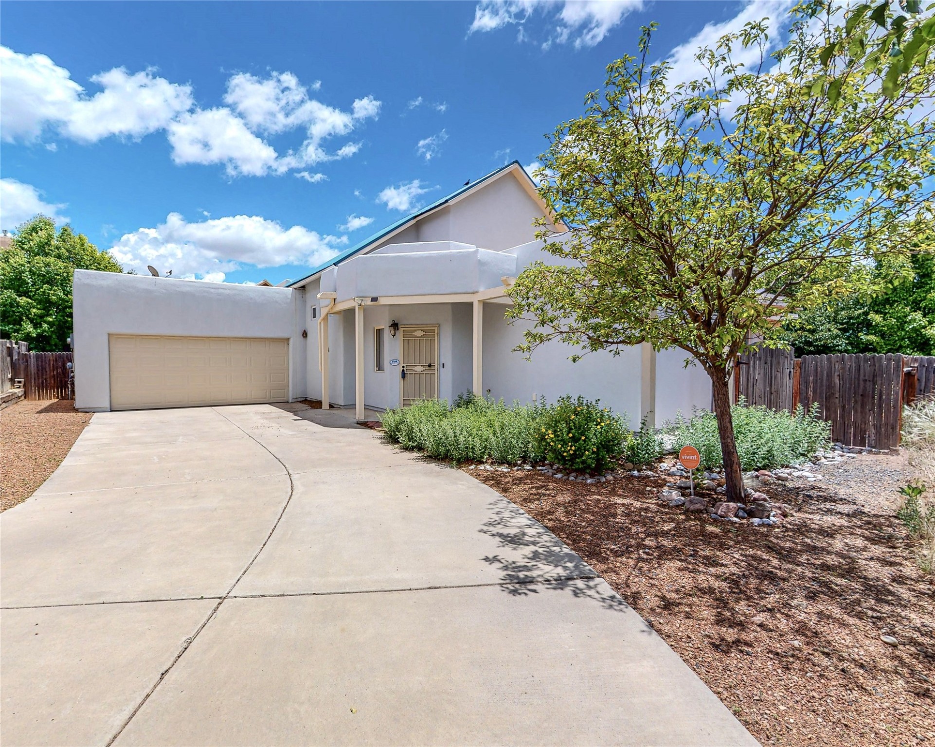 Stucco home with a two-car garage, curved driveway, covered entry, and leafy tree.