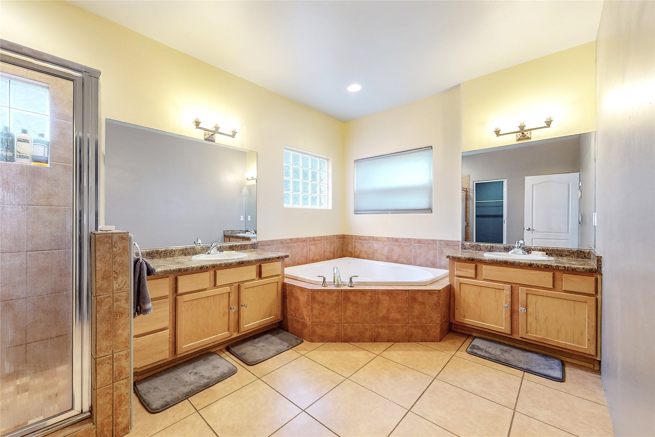 Bathroom with a corner soaking tub, double wood vanities, granite counters, and a glass-enclosed tiled shower.