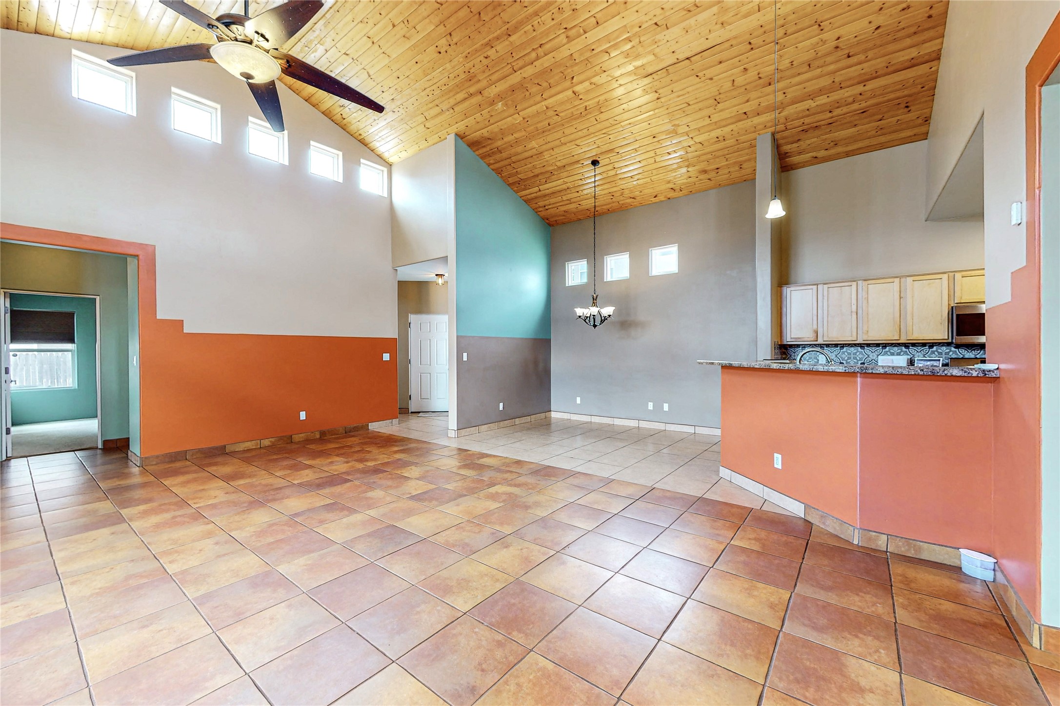 Open-plan living and dining area with vaulted wood ceiling, terracotta tile, and kitchen breakfast bar.