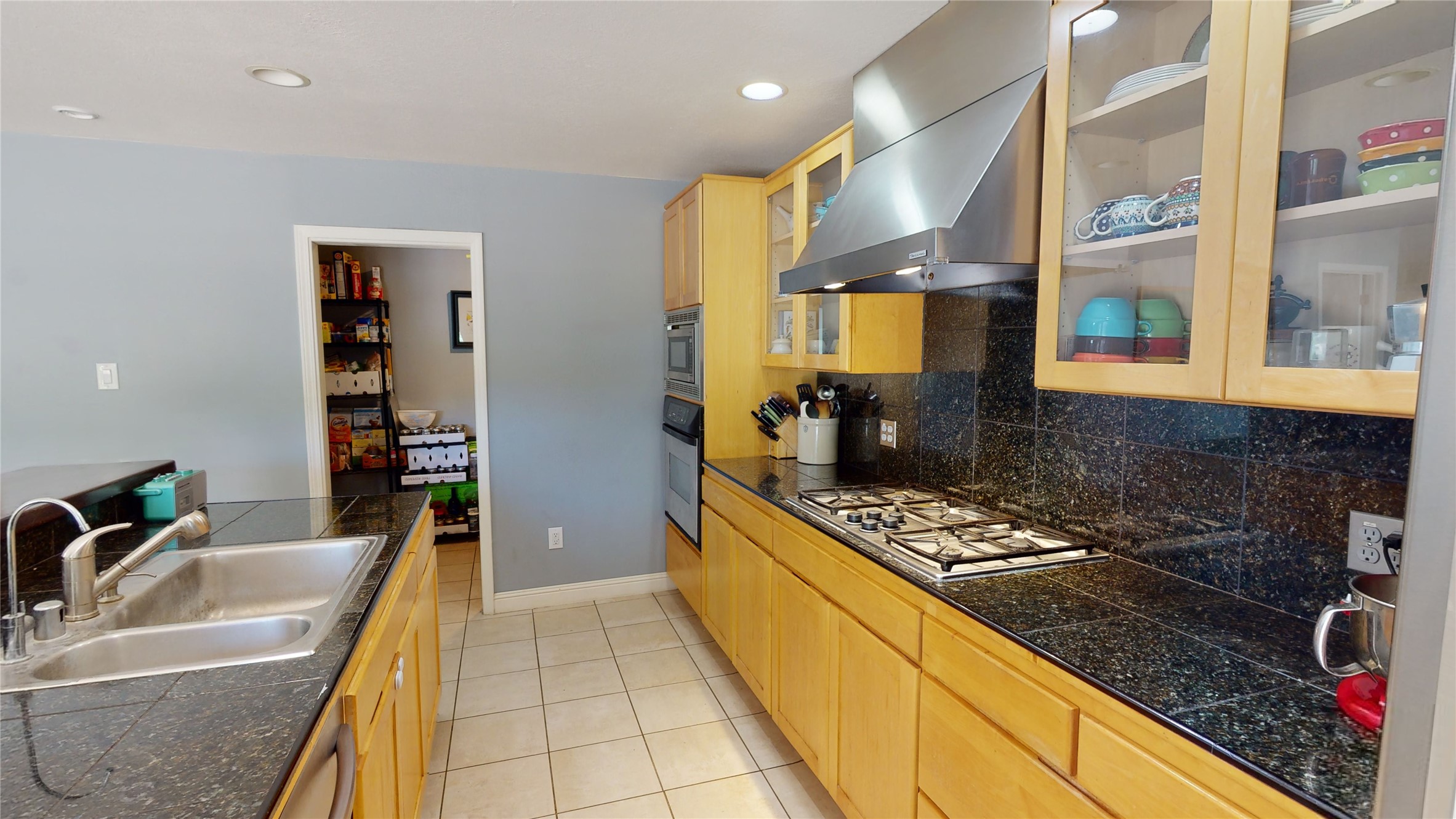 Kitchen with light wood cabinets, dark granite counters, gas cooktop, and double-basin sink.