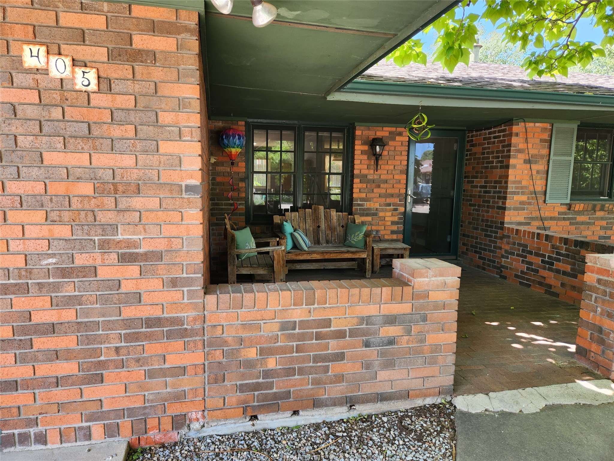 Brick home’s covered front porch with rustic seating beneath a green roof.