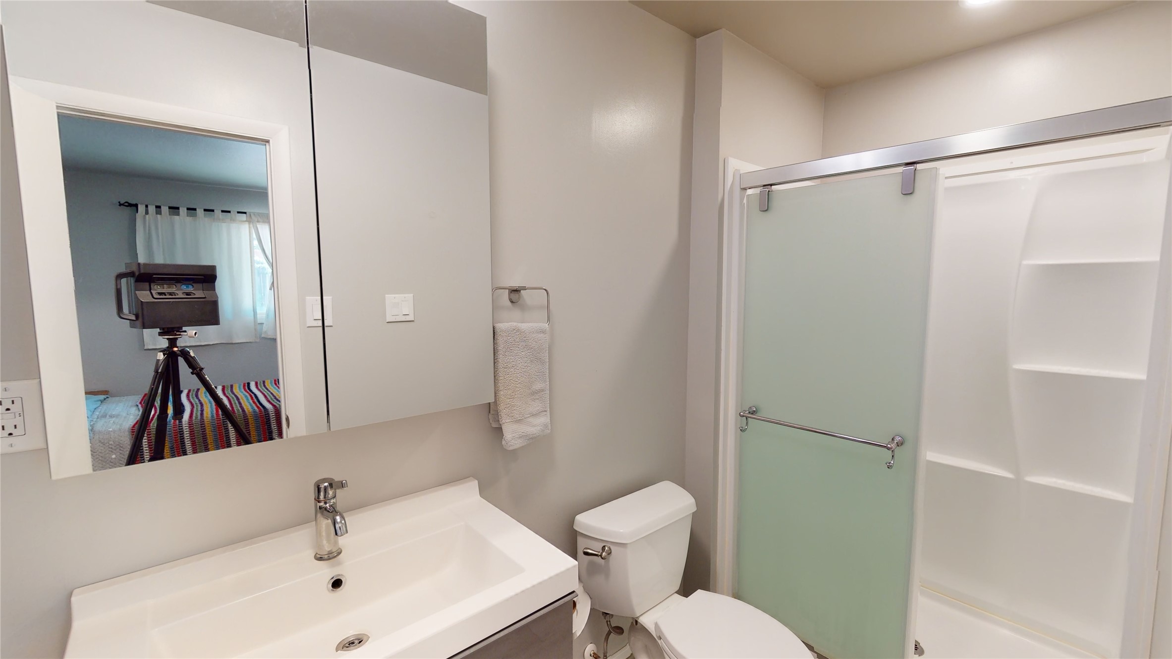 Bathroom with a white sink vanity, toilet, and frosted glass shower door beside built-in shelves.