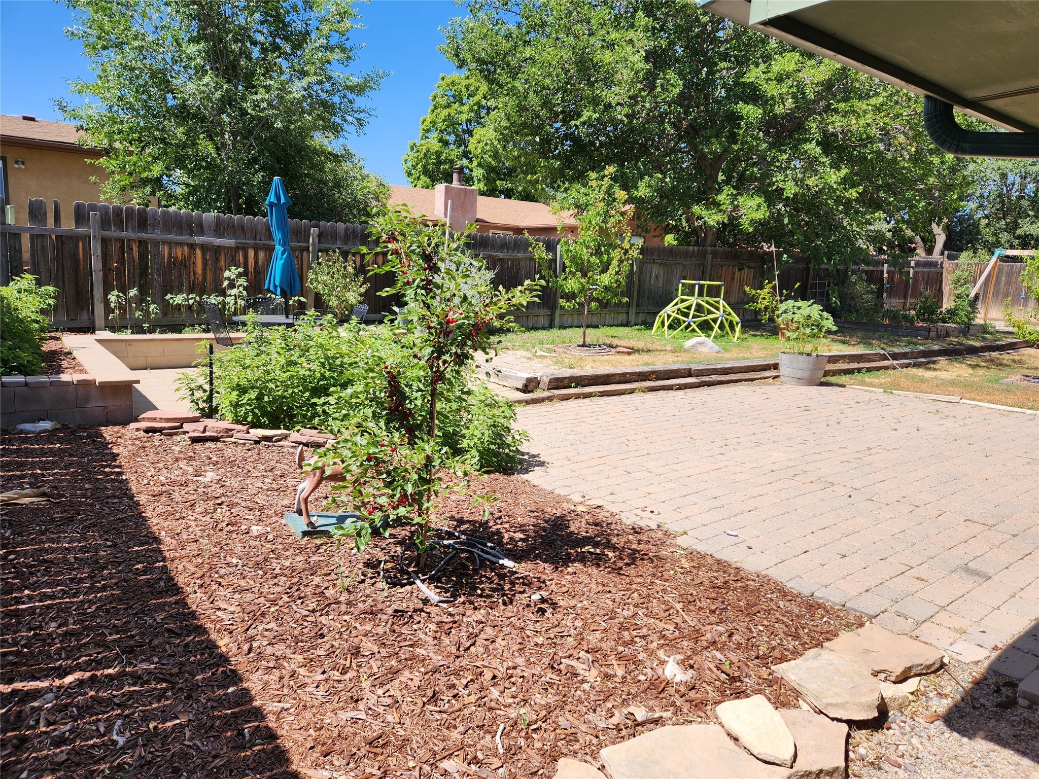 Backyard with a spacious paver patio, fenced garden beds, and a small climbing structure.
