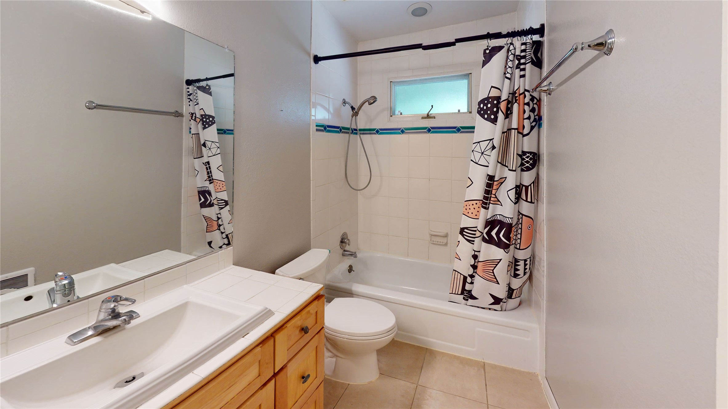 Bathroom with tiled vanity, wood cabinetry, and a bathtub behind a patterned shower curtain.