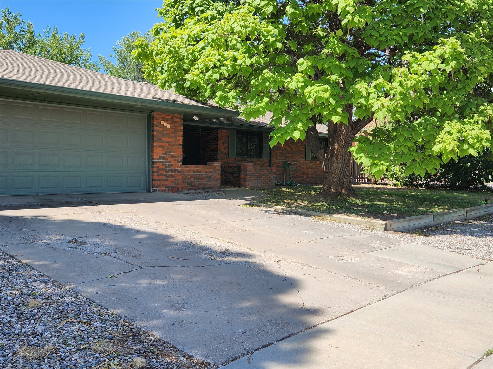 Brick ranch-style home with a wide garage, concrete driveway, and large shade tree.