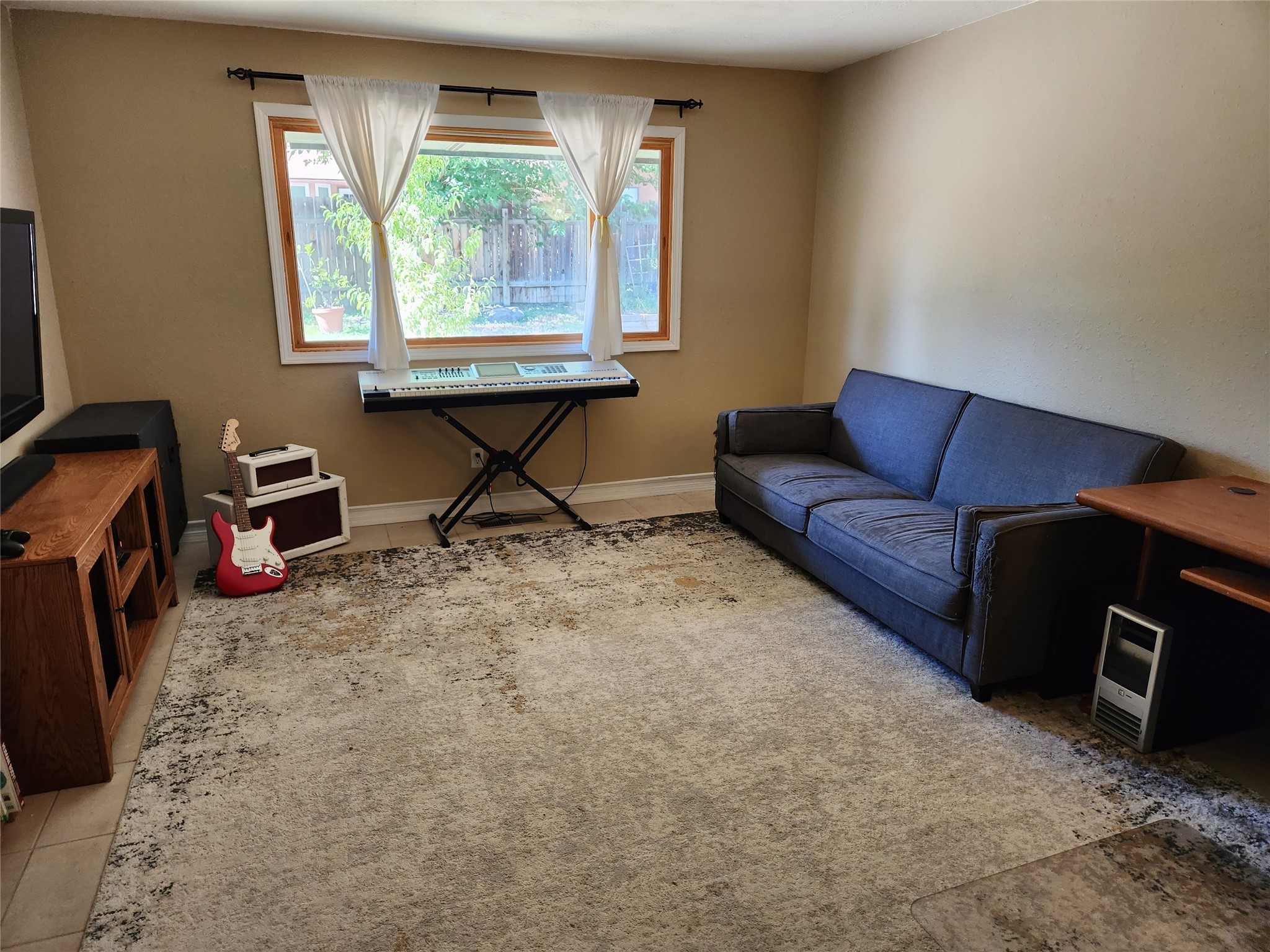 Living room with blue sofa, keyboard, red electric guitar, and large curtained window.