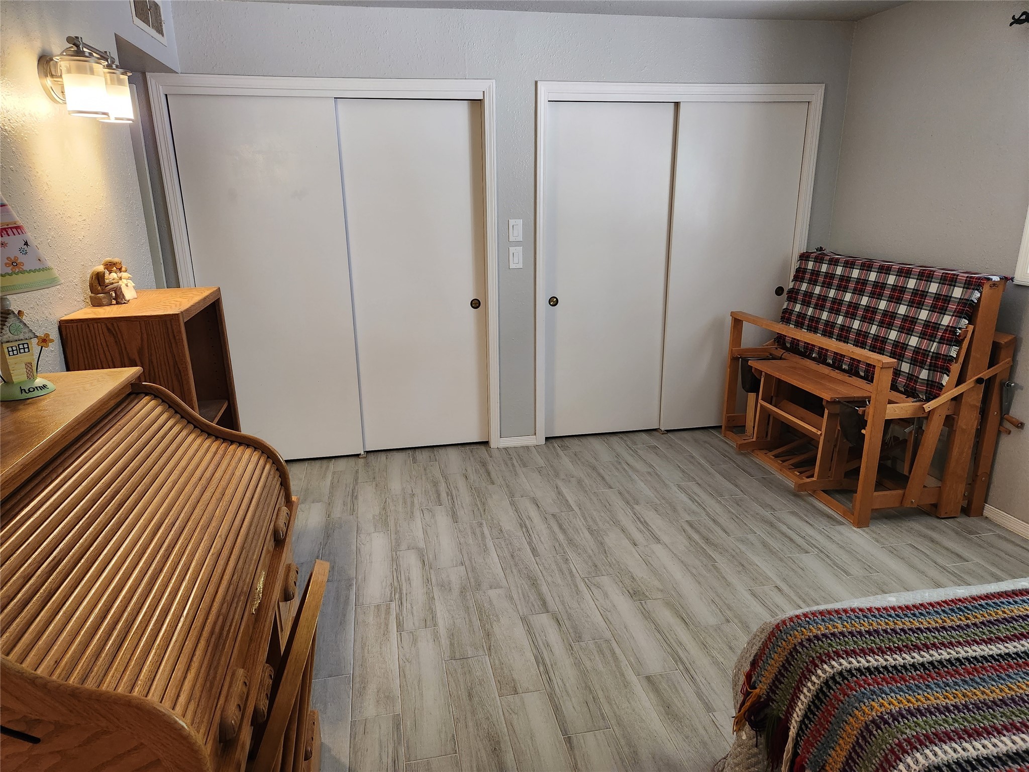 Bedroom with gray tile flooring, sliding closets, and wooden bed and futon.