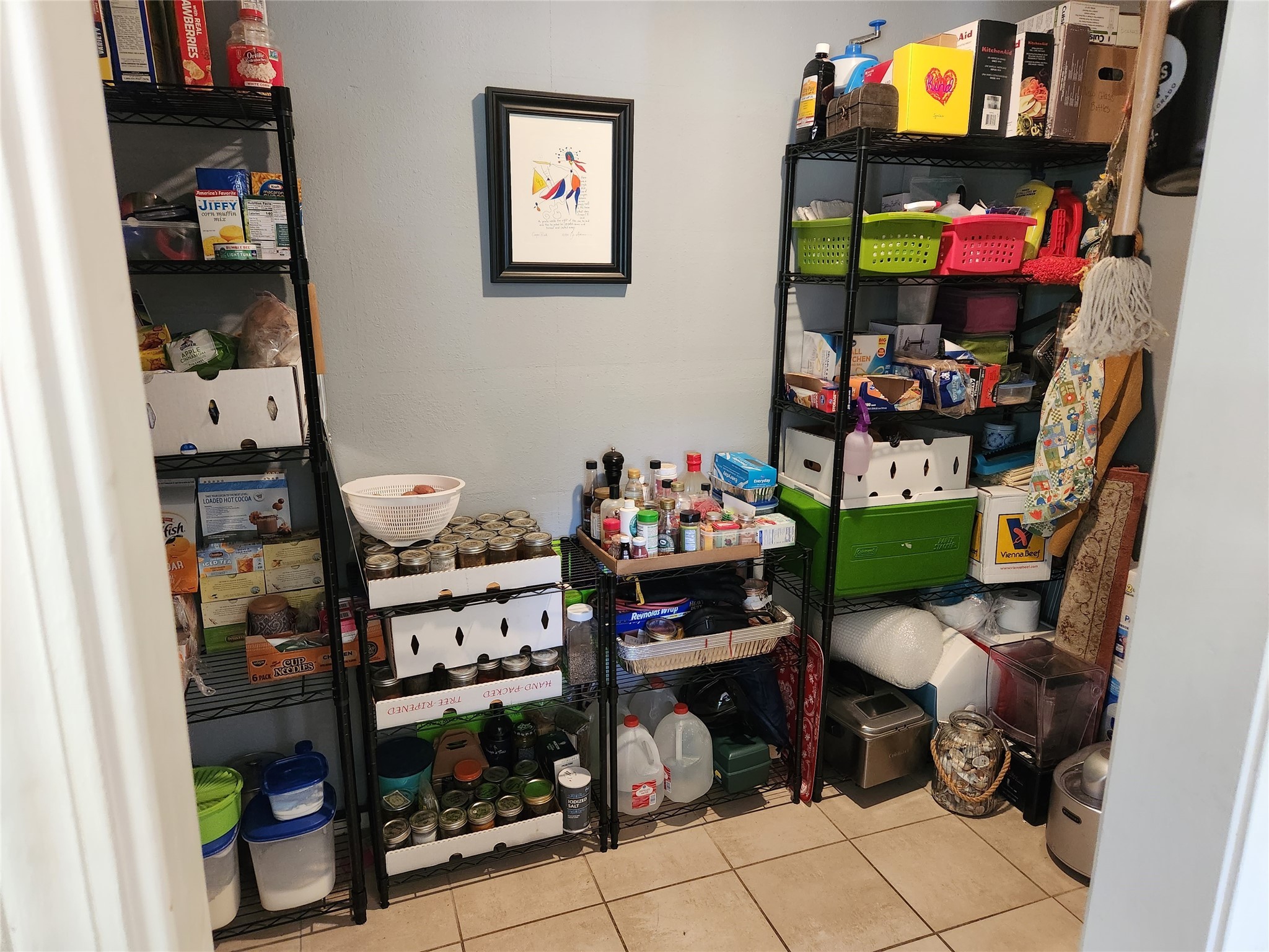 Pantry with crowded wire shelves holding food, canned goods, containers, and household supplies.