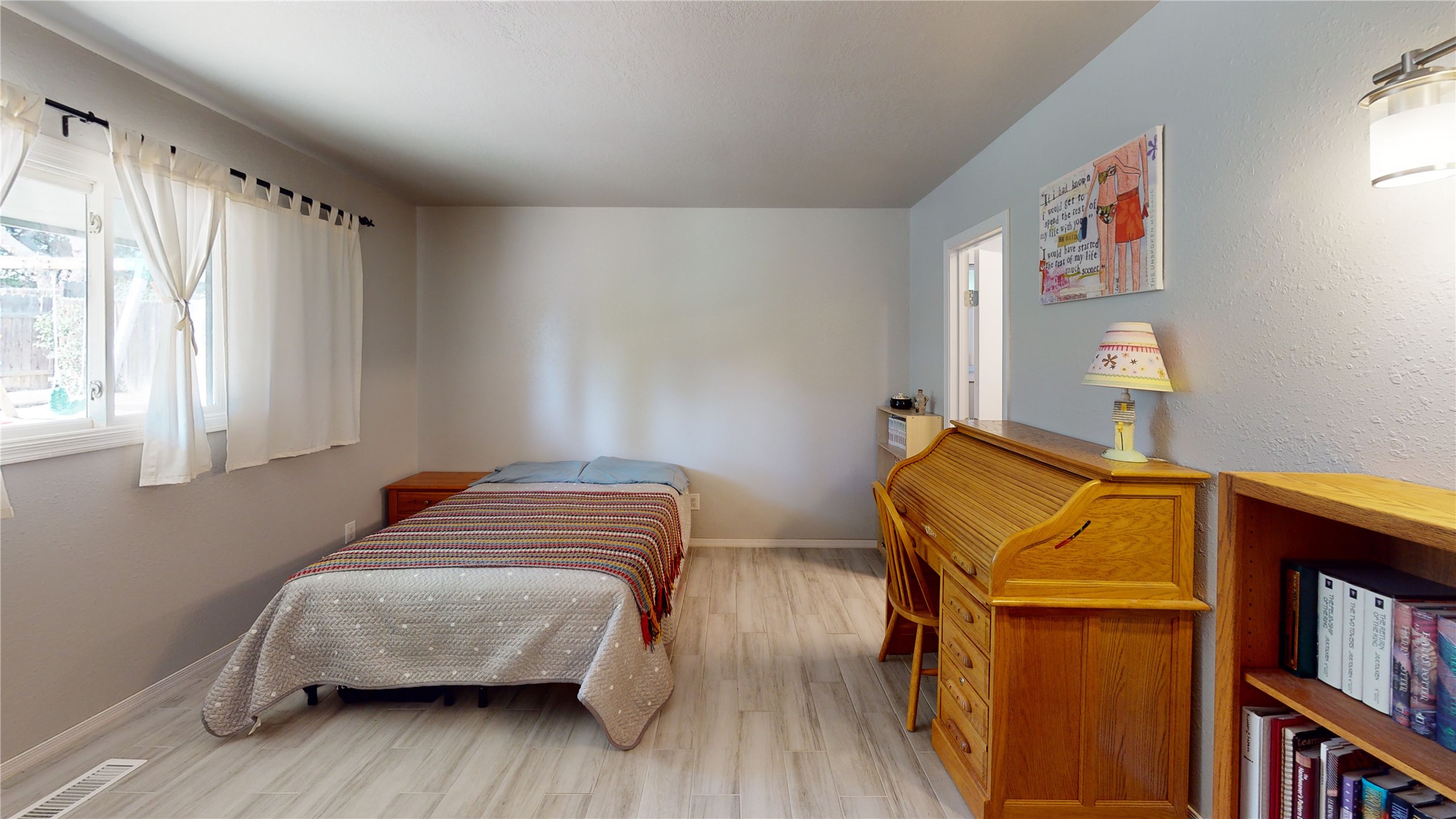 Furnished bedroom with a single bed, curtained window, and wooden roll-top desk.