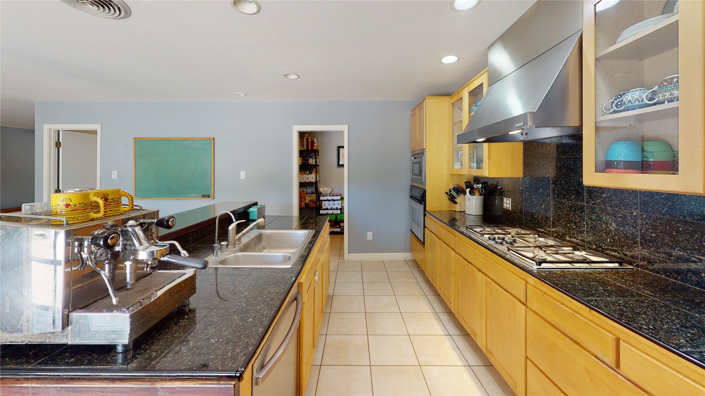 Kitchen with honey-colored cabinets, dark granite counters, gas cooktop, and a large espresso machine.
