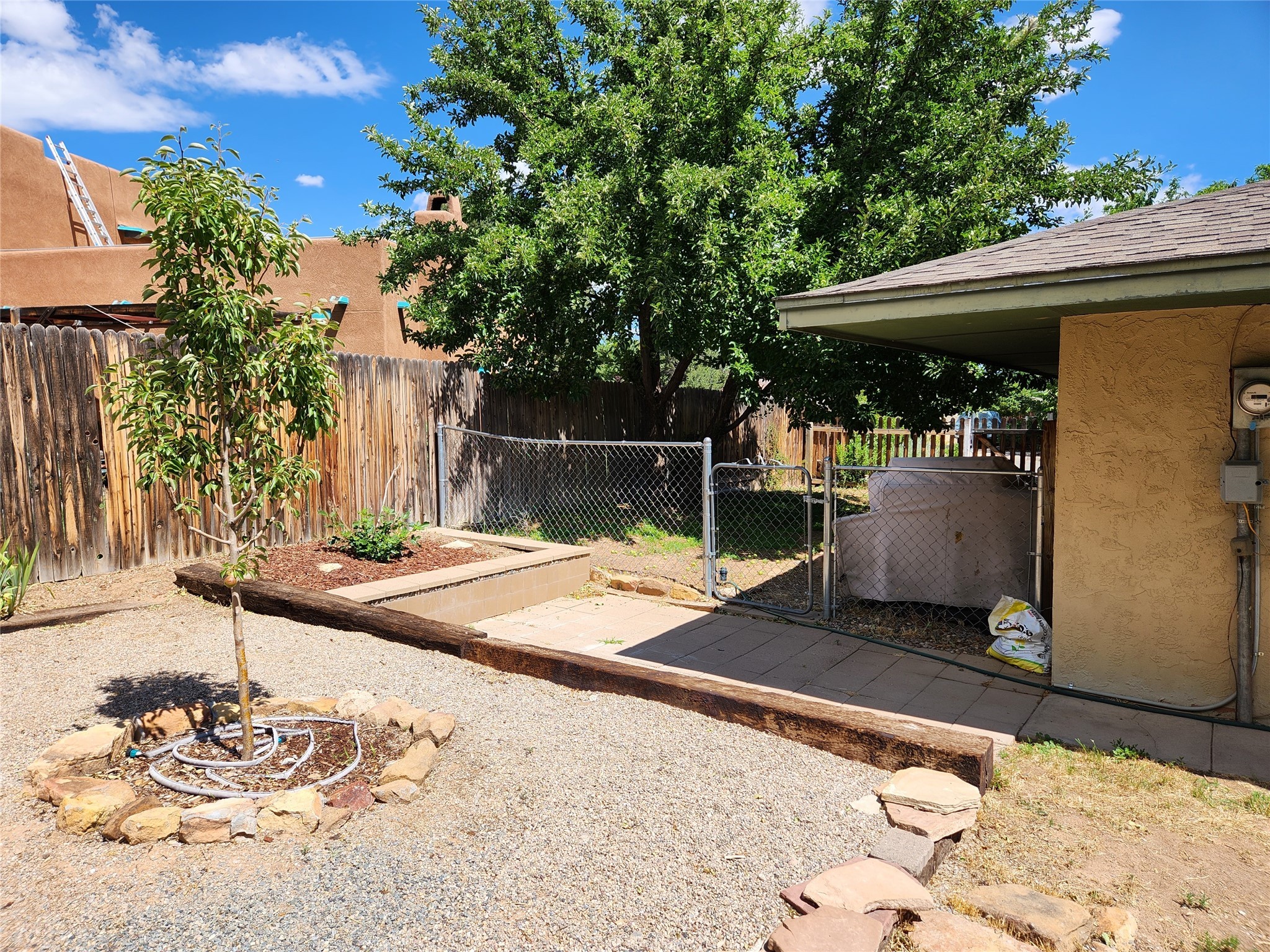 Backyard with a gravel yard, stone-edged tree bed, fenced area, and covered patio.