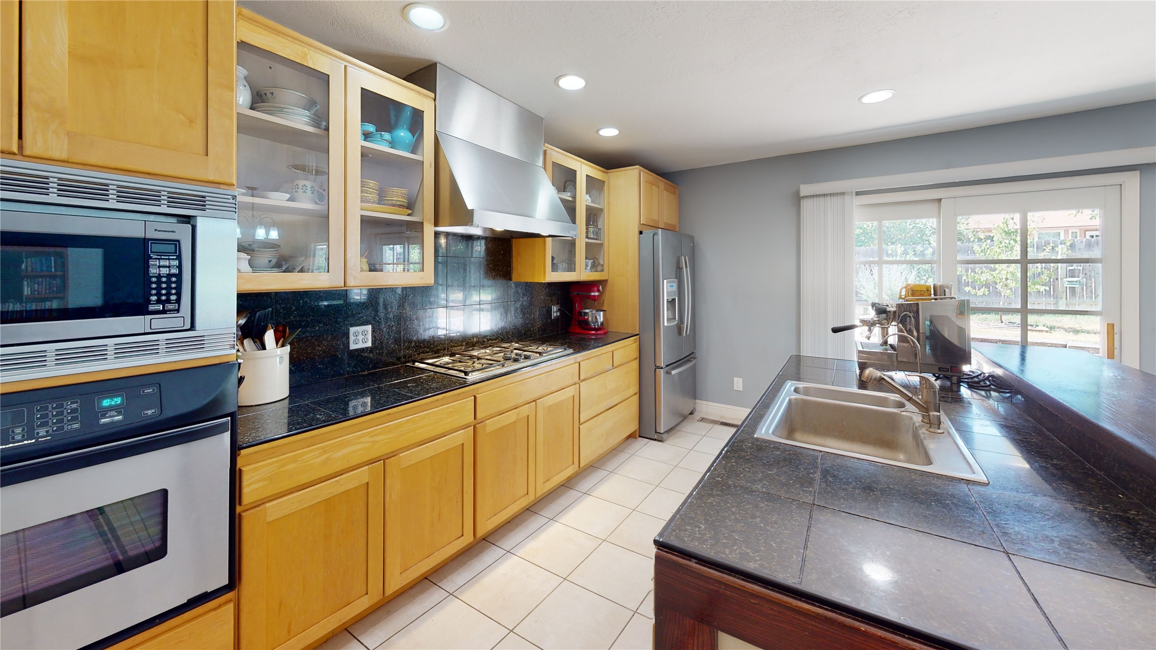 Kitchen with honey-colored wood cabinets, dark granite counters, stainless steel appliances, and a large island sink.