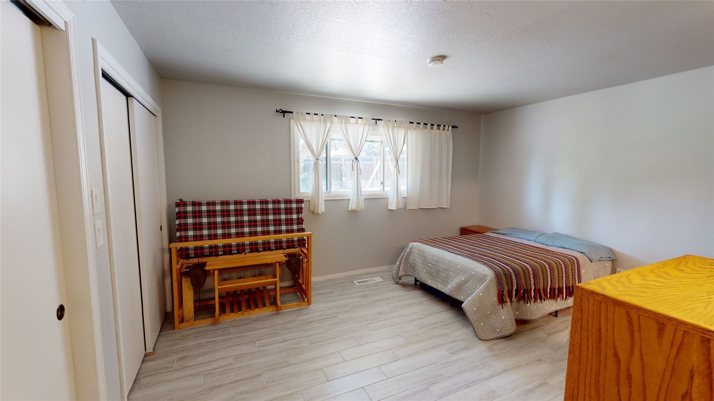Bedroom with a patterned bedspread, plaid futon, and curtained window.