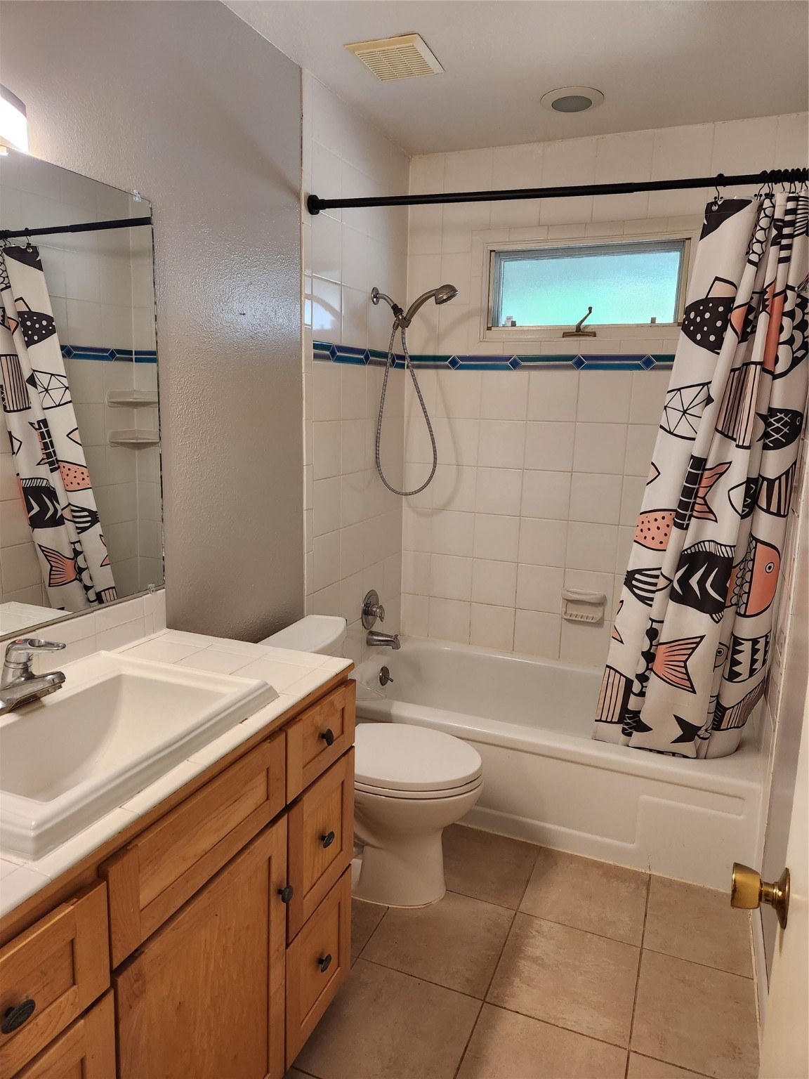 Bathroom with a tiled tub and shower, patterned curtain, and wood vanity.