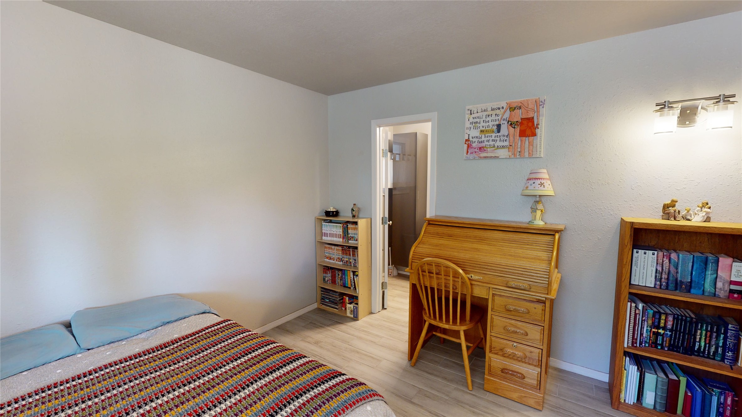 Bedroom with colorful striped bedcover, wooden rolltop desk, and bookcases.