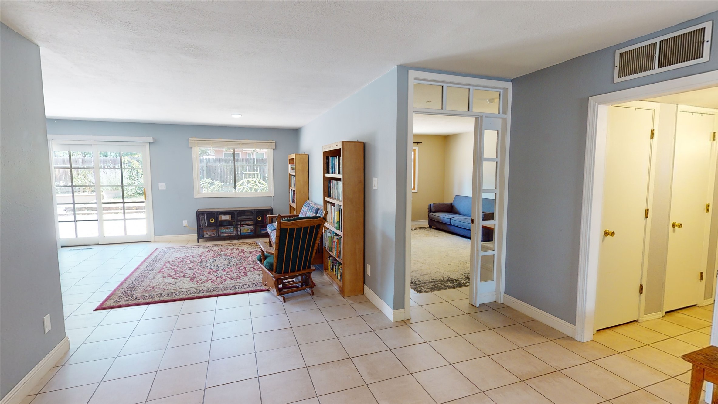 Living room with a patterned rug, bookshelves, rocking chair, and sliding glass doors.