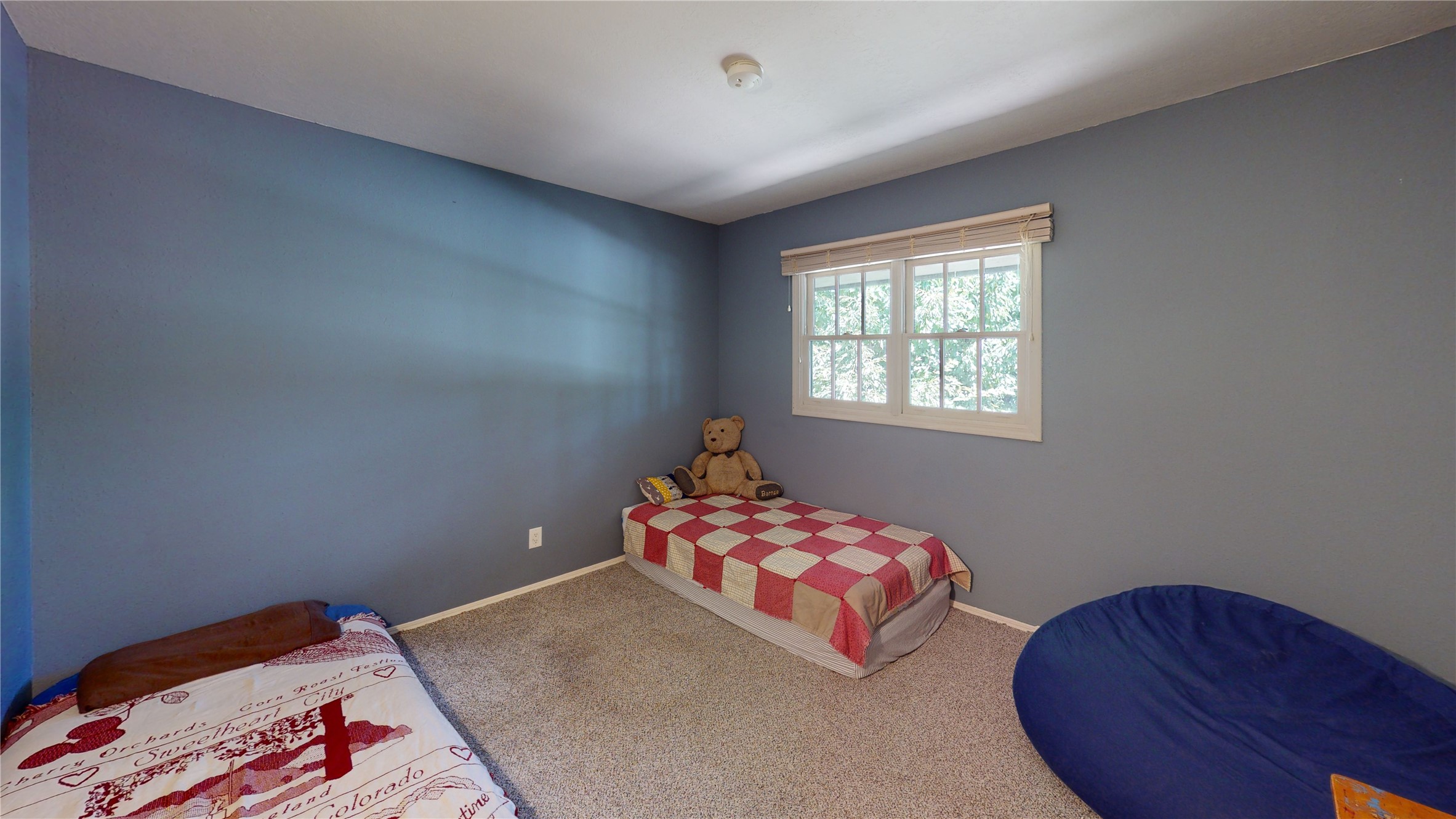 Bedroom with blue-gray walls, two single beds, a teddy bear, and a window with blinds.
