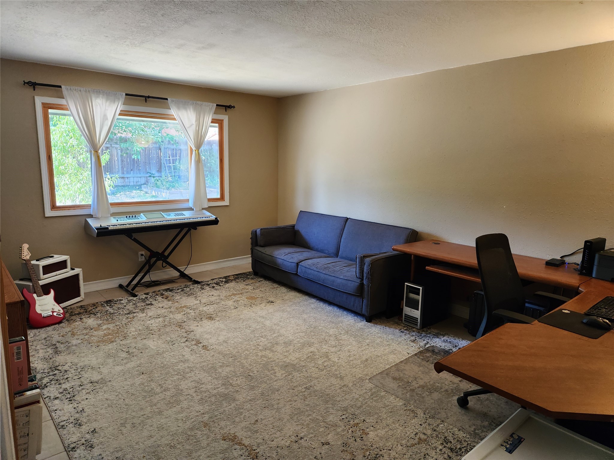 Furnished home office with a blue sofa, wooden desk, digital keyboard, and red electric guitar.