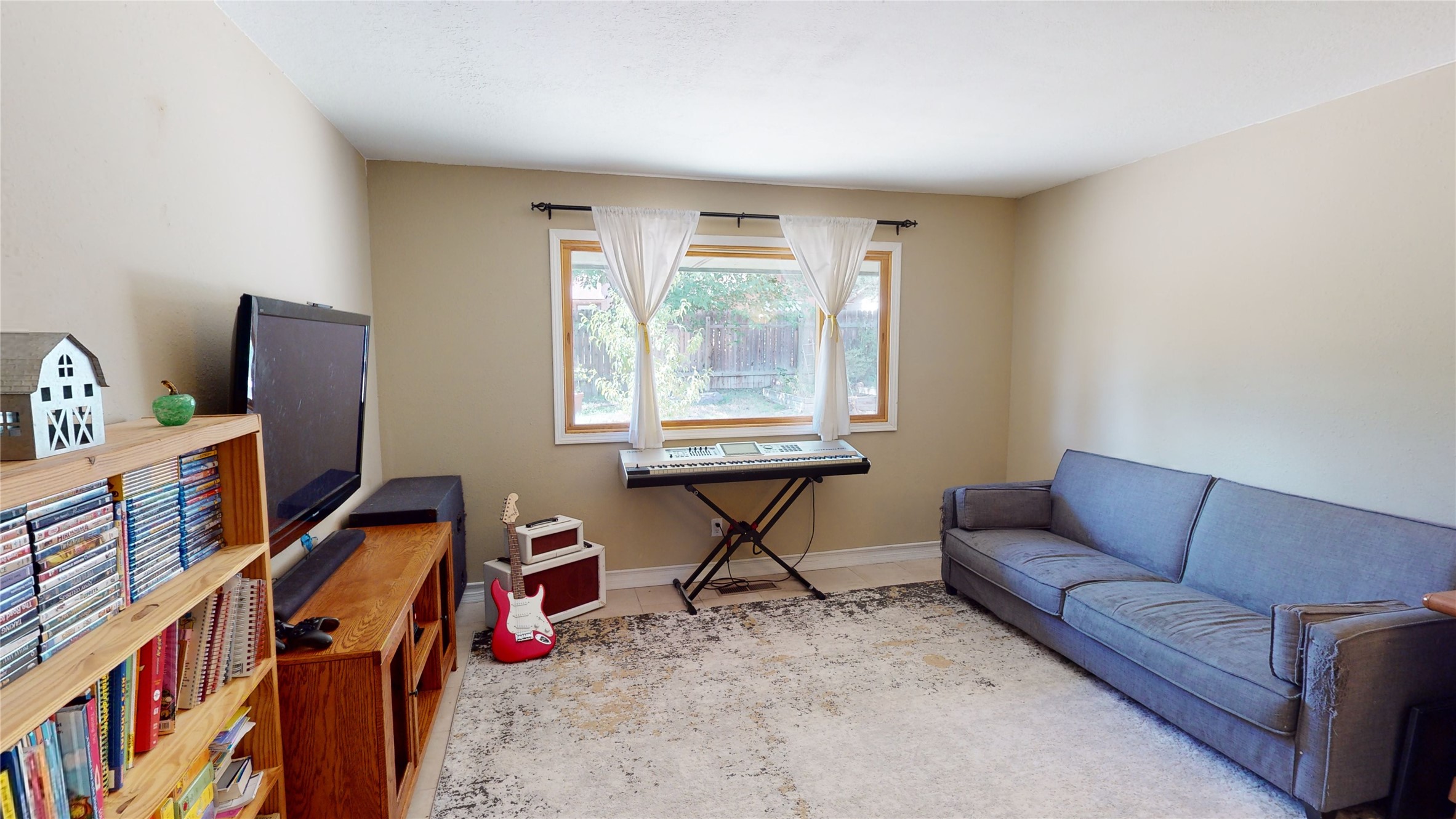 Music room with blue-gray sofa, keyboard beneath a window, red electric guitar, and wooden media shelving.