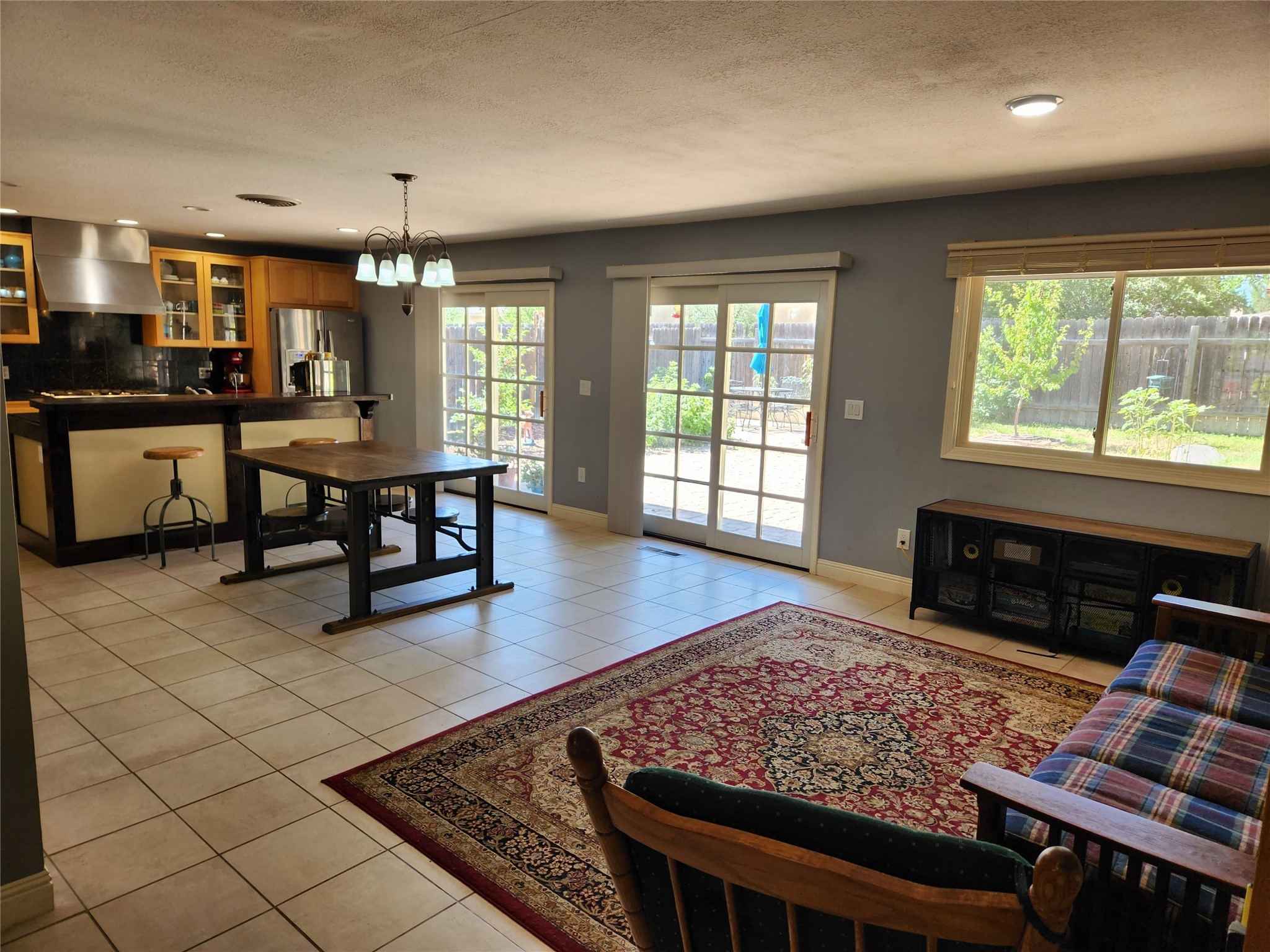 Open-plan living and dining area with a tiled floor, wood kitchen cabinets, and glass doors to the backyard.