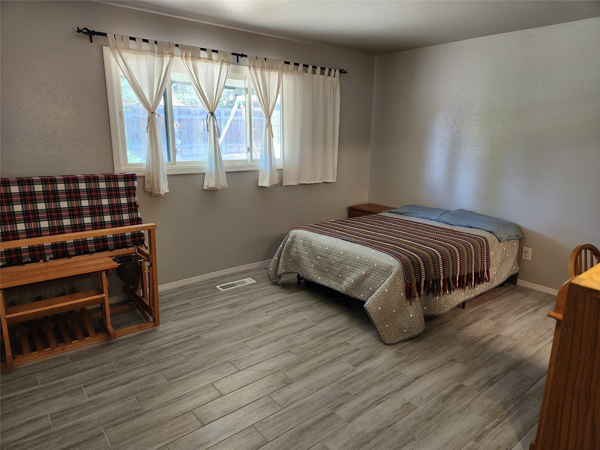 Bedroom with a patterned bedspread, plaid futon, gray tile floor, and curtained window.