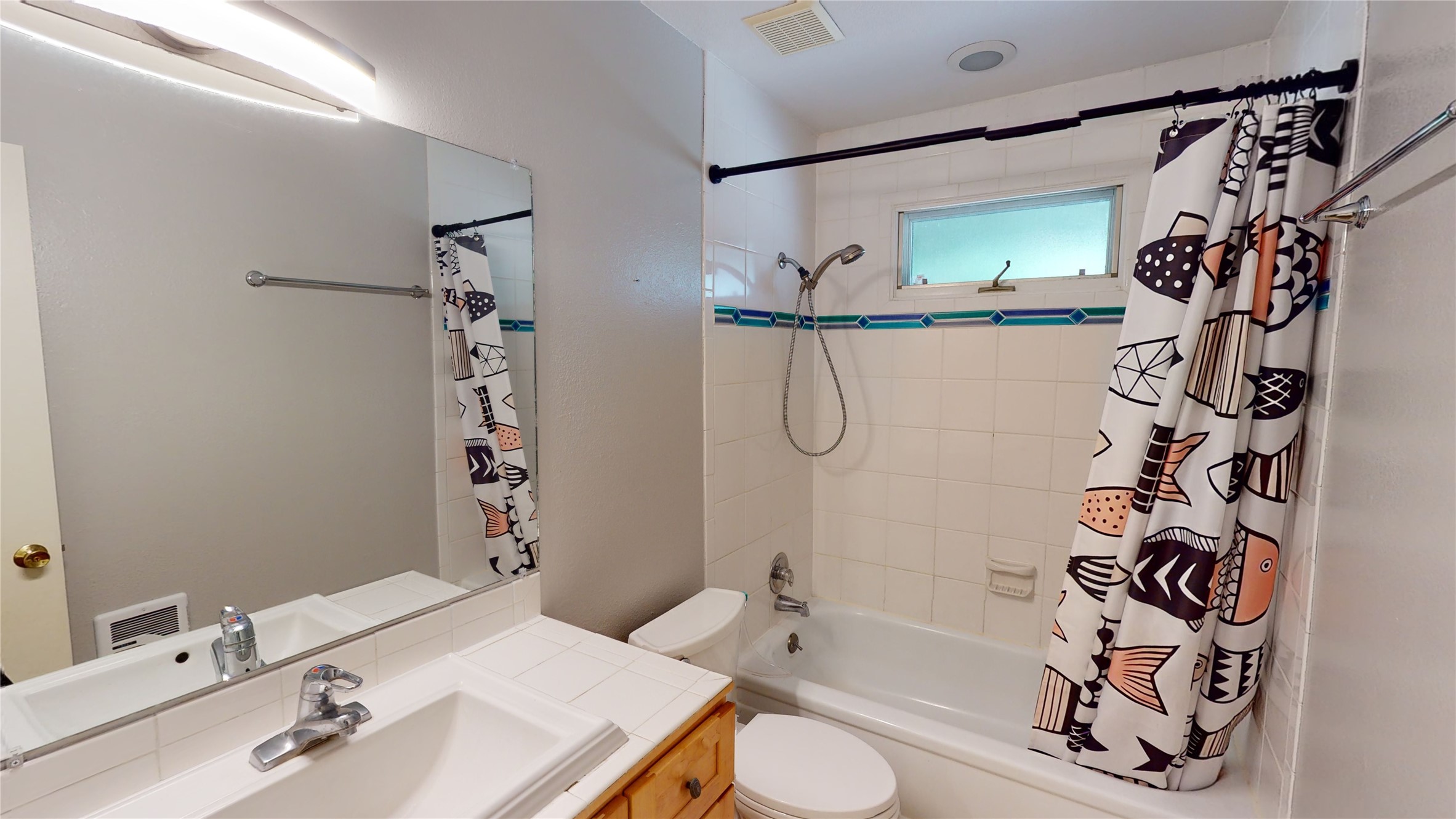 Bathroom with tiled vanity, bathtub, frosted window, and patterned shower curtain.