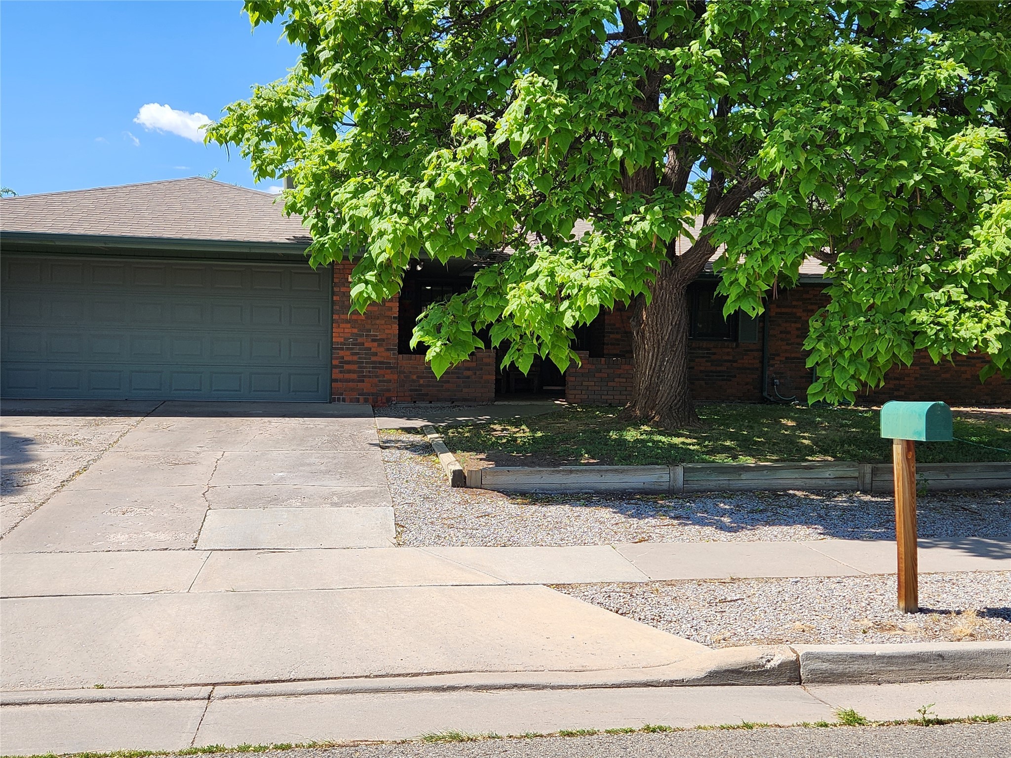 Brick home with a two-car garage, broad driveway, and large leafy tree in front.