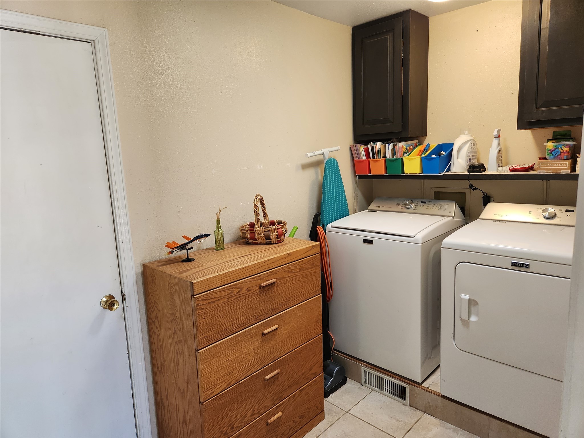 Laundry room with Maytag washer and dryer, colorful storage bins, and a wooden chest of drawers.