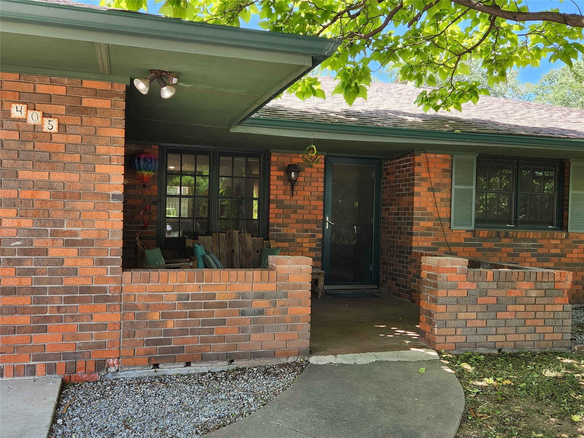 Red brick home with a covered porch, wooden bench, and curved walkway to the entry.