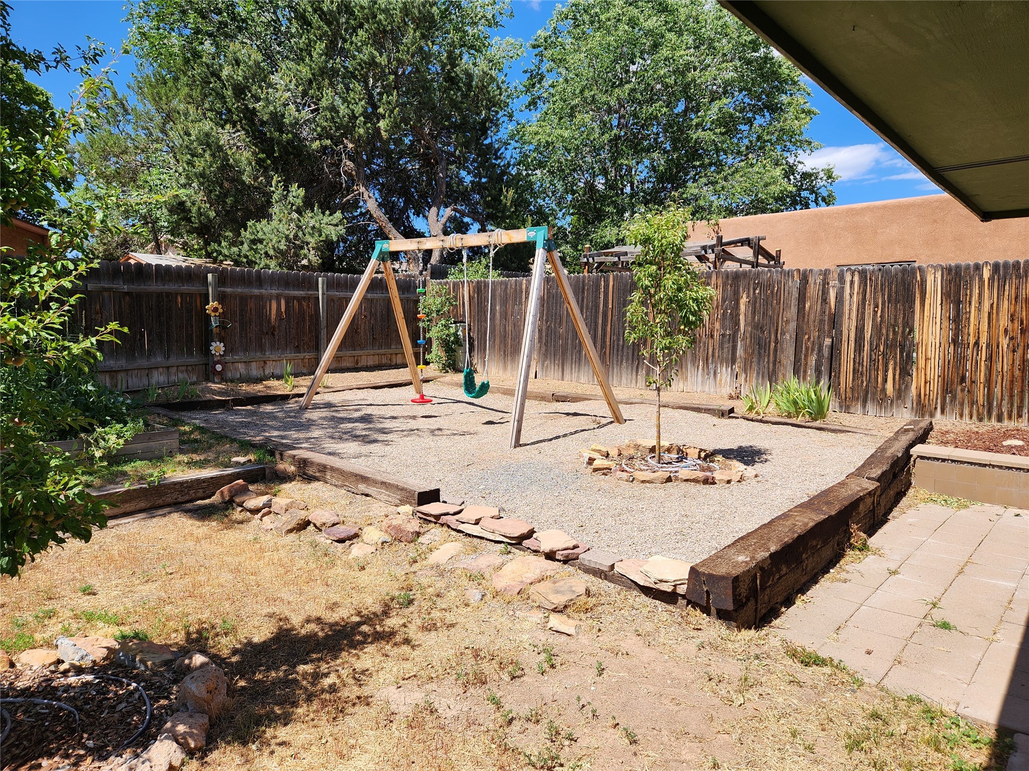 Backyard play area with a wooden swing set, gravel ground, and tall wooden fencing.