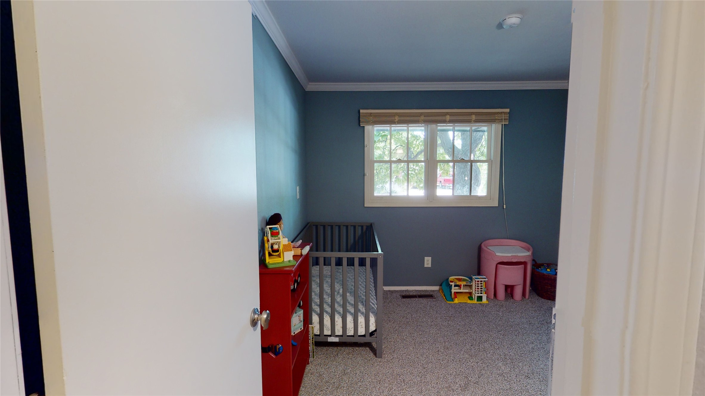 Nursery with a gray crib, blue walls, toys, and a bright window.