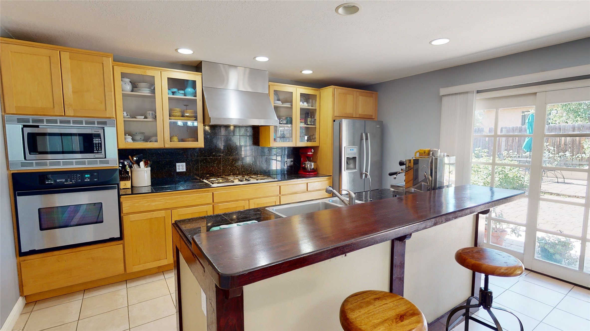 Kitchen with honey-colored cabinets, stainless appliances, and a large island breakfast bar beside patio doors.