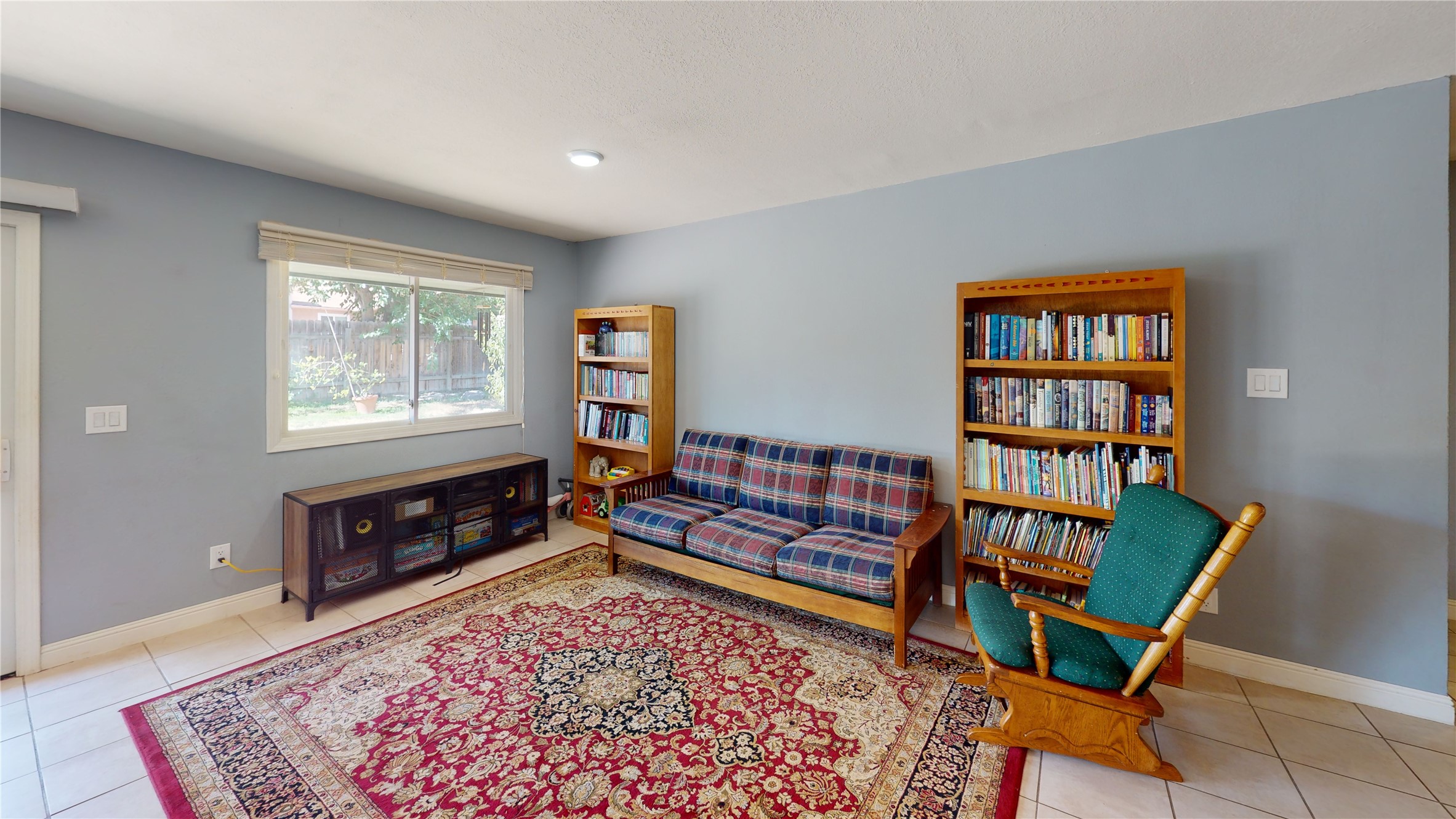 Furnished living room with bookcases, plaid sofa, rocking chair, and large patterned rug.
