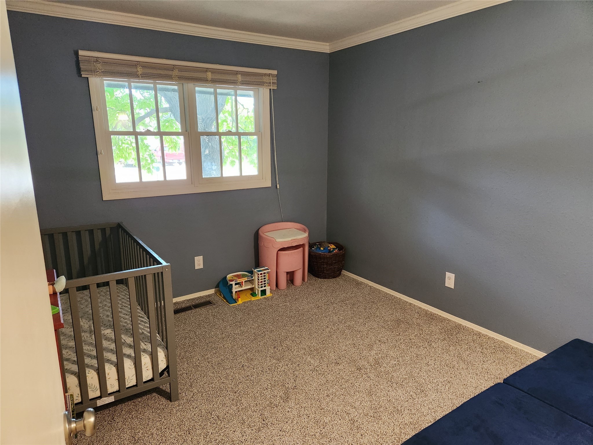 Nursery with a dark crib, toys, and a pink table beneath a window.