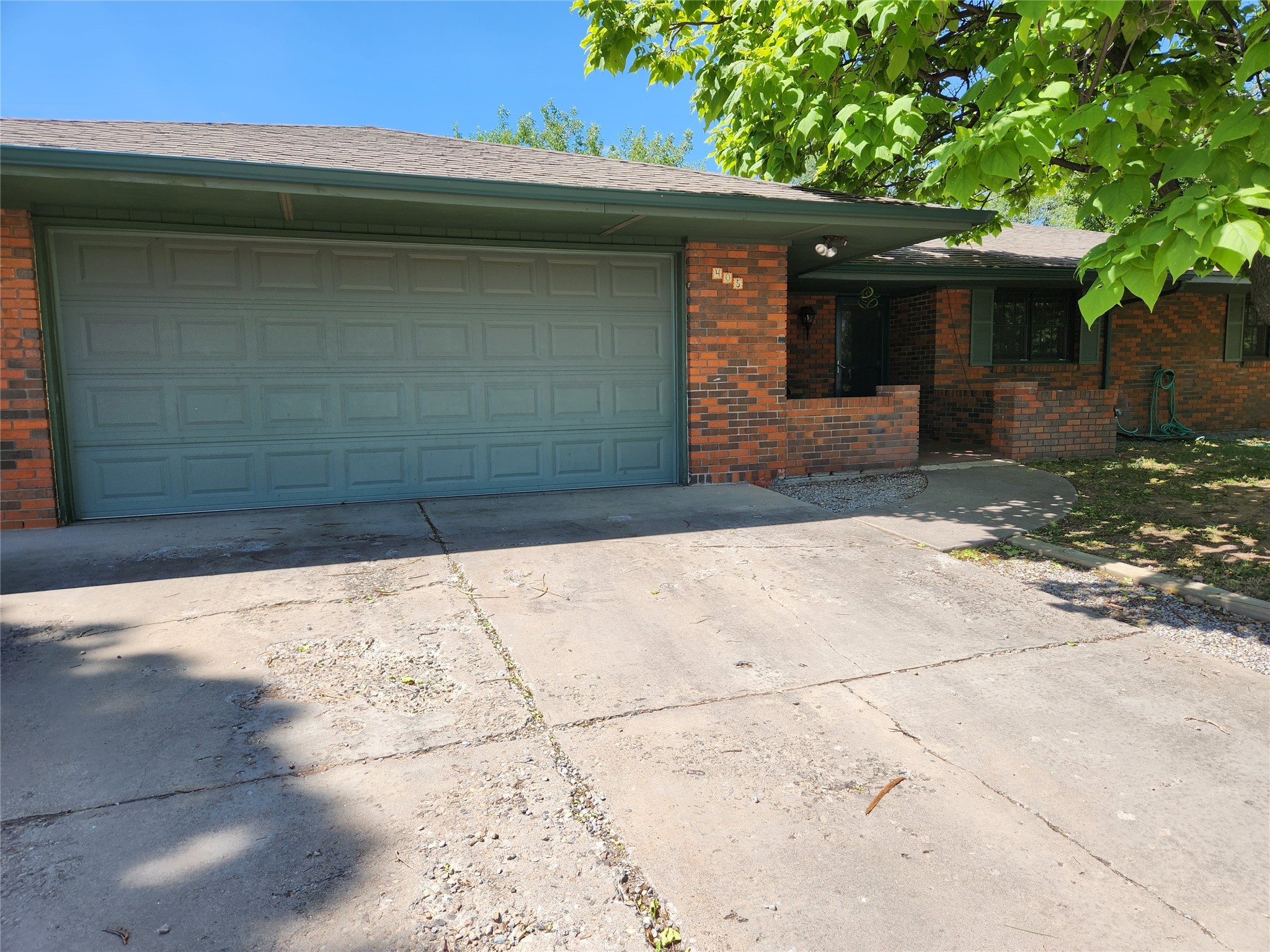 Brick home with a wide gray double garage door and a leafy tree shading the driveway.