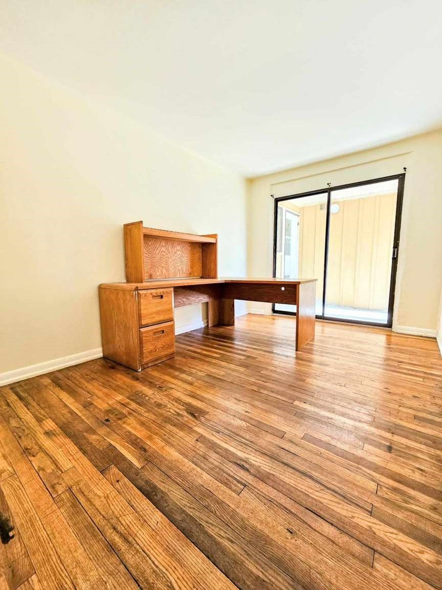 Room with polished wood floors, a wooden desk and hutch, and sliding glass doors.