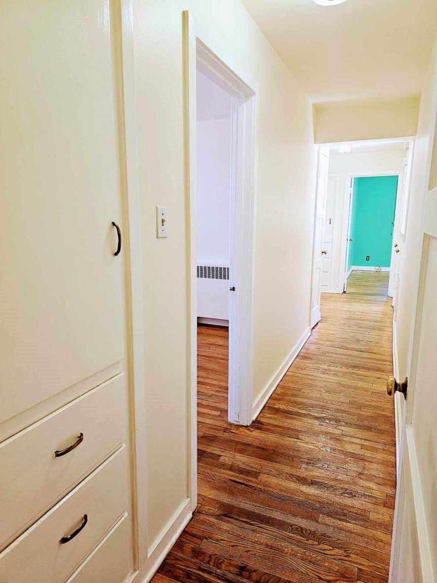 Hallway with hardwood floors, built-in drawers, and a turquoise wall at the far end.